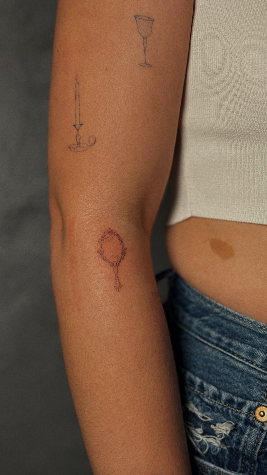 Four tattoos on person's arm: a wine glass, a candle, a circle with a line, and a magnifying glass.