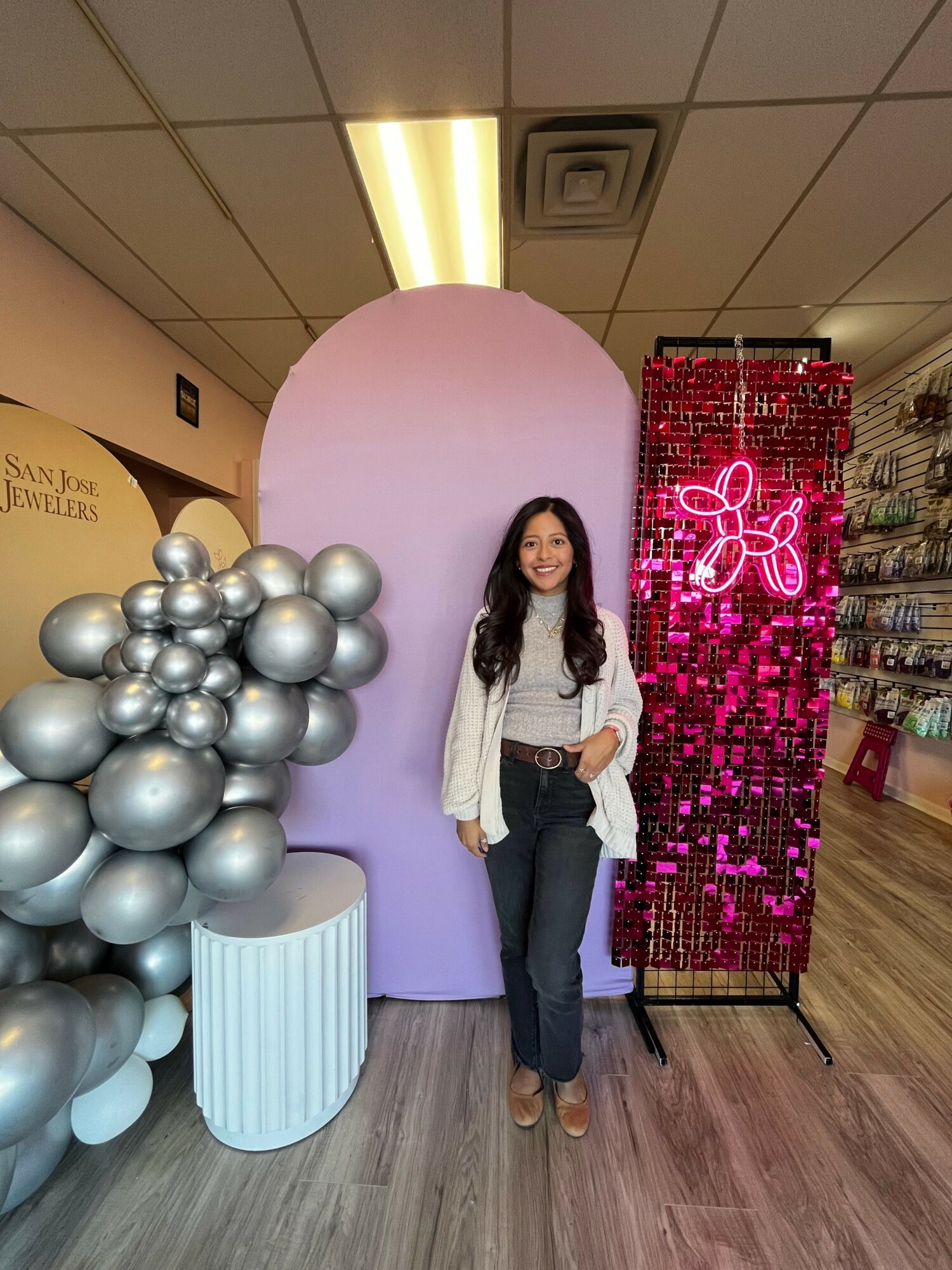 Woman standing next to pink and silver balloon display with a pink neon butterfly sign in background.