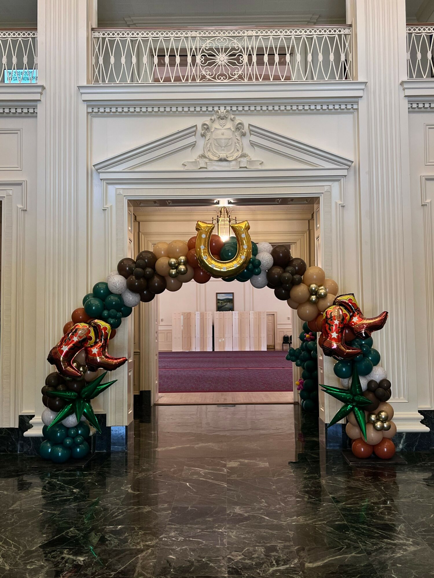 Decorative balloon arch with gold, black, and metallic balloons, including star-shaped balloons, in front of a white wall with architectural details.