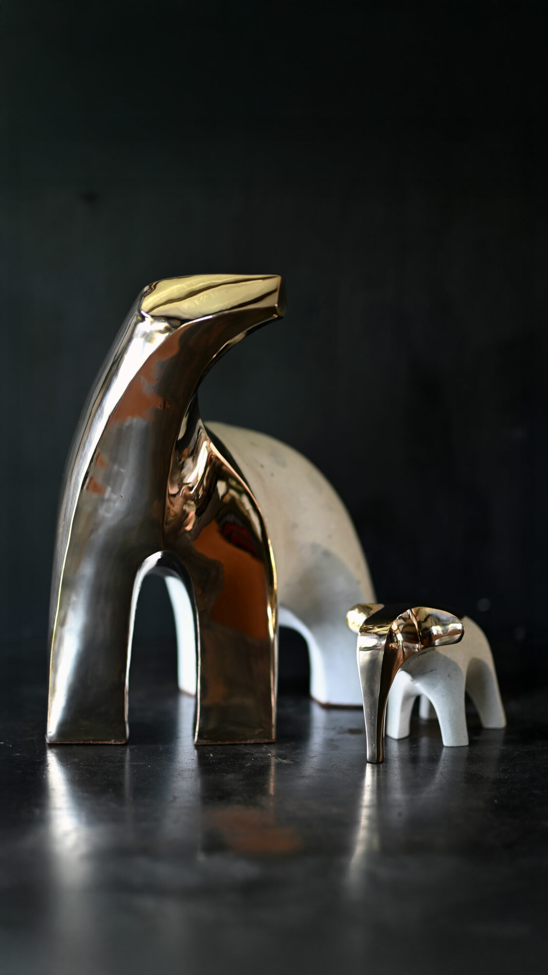 Two metallic animal-shaped sculptures, one larger and one smaller, on a dark surface with a dark background.