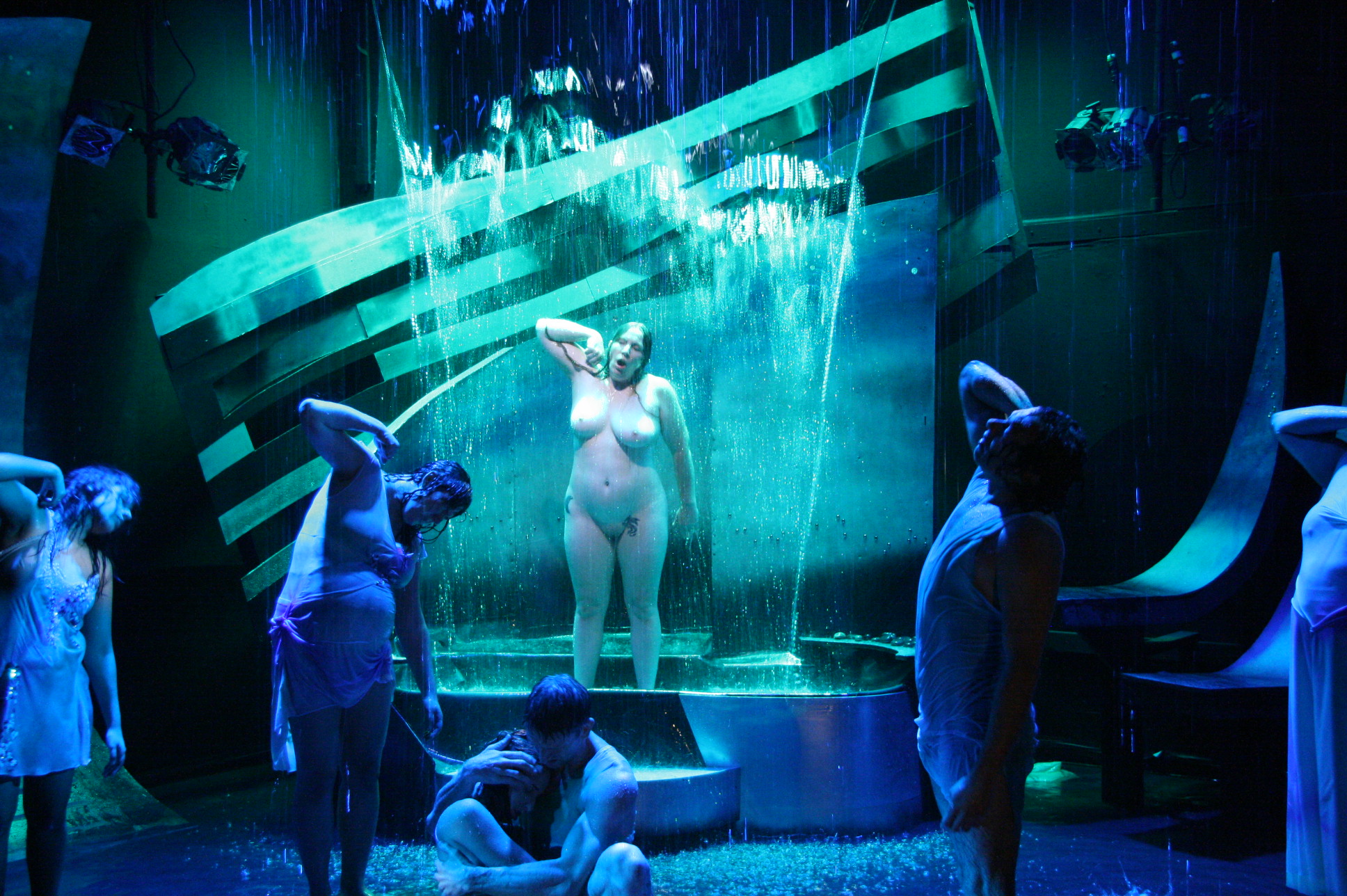 Group of children around a fountain with a statue of a woman, illuminated by blue and green lights, in a dark setting.