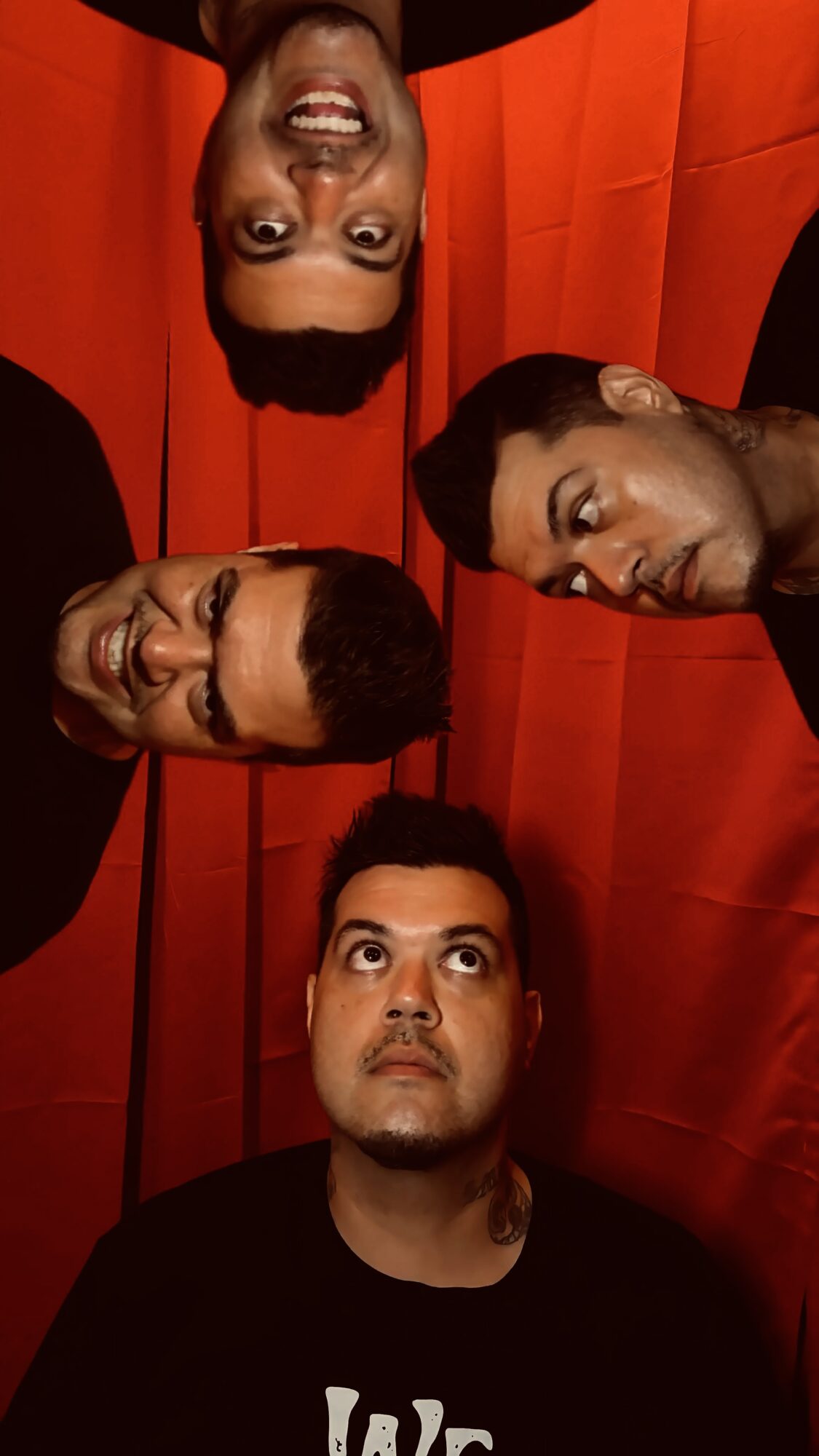 Four people with heads close together, looking up at the camera, against a red background.
