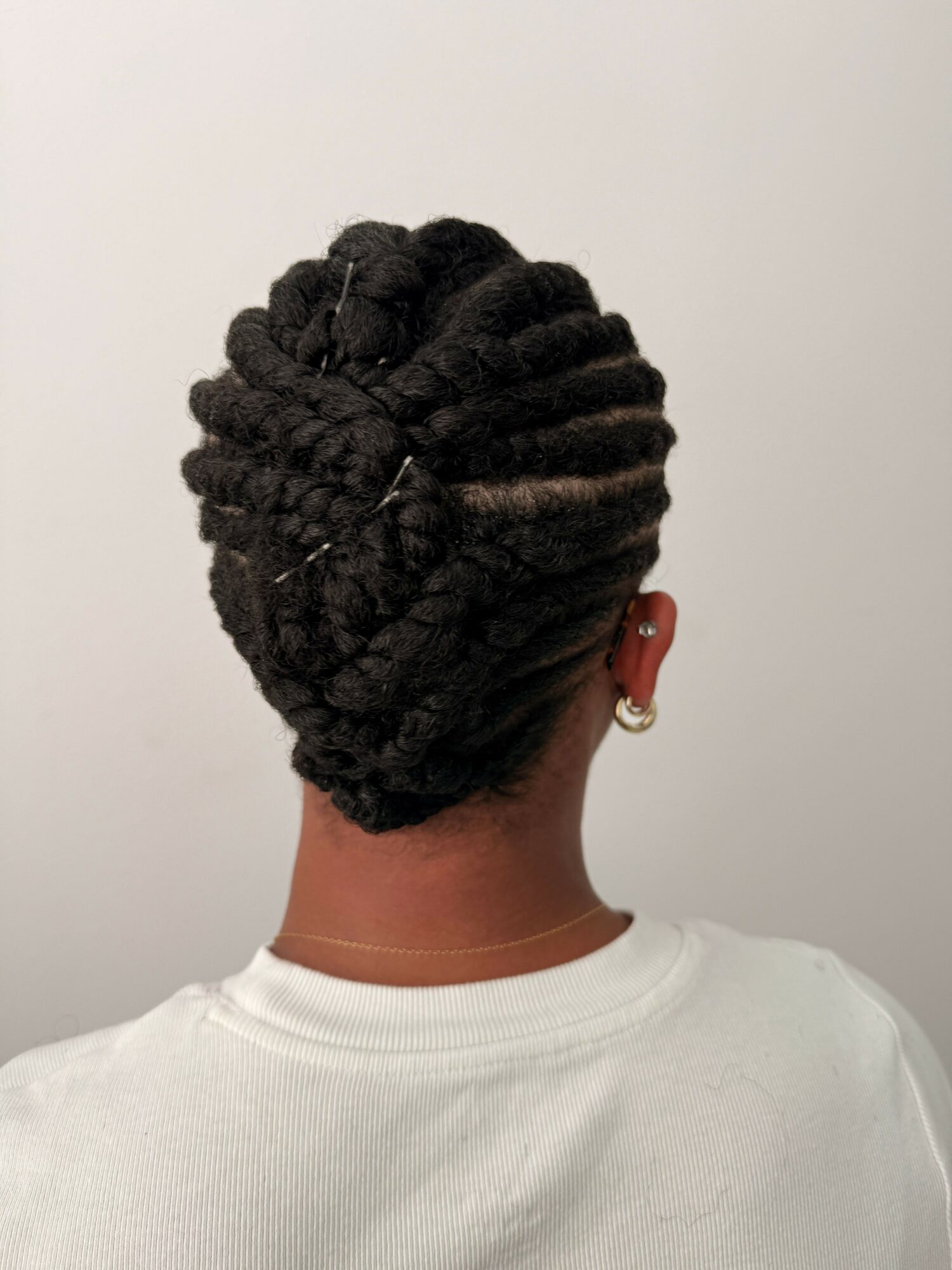 Person with styled dreadlocks facing sideways, wearing a white shirt, against a plain background.
