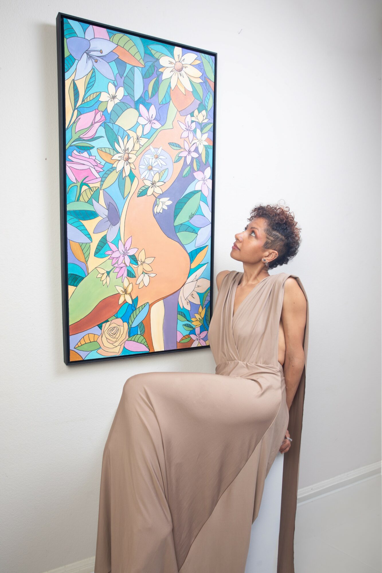 Woman sitting on a white chair looking at a colorful abstract painting on the wall.