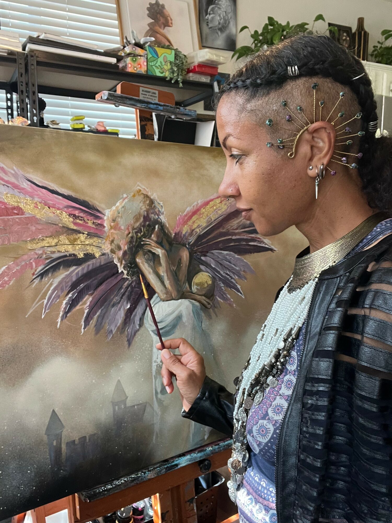 Woman with elaborate hairstyle and earrings painting a colorful bird on canvas in an art studio.