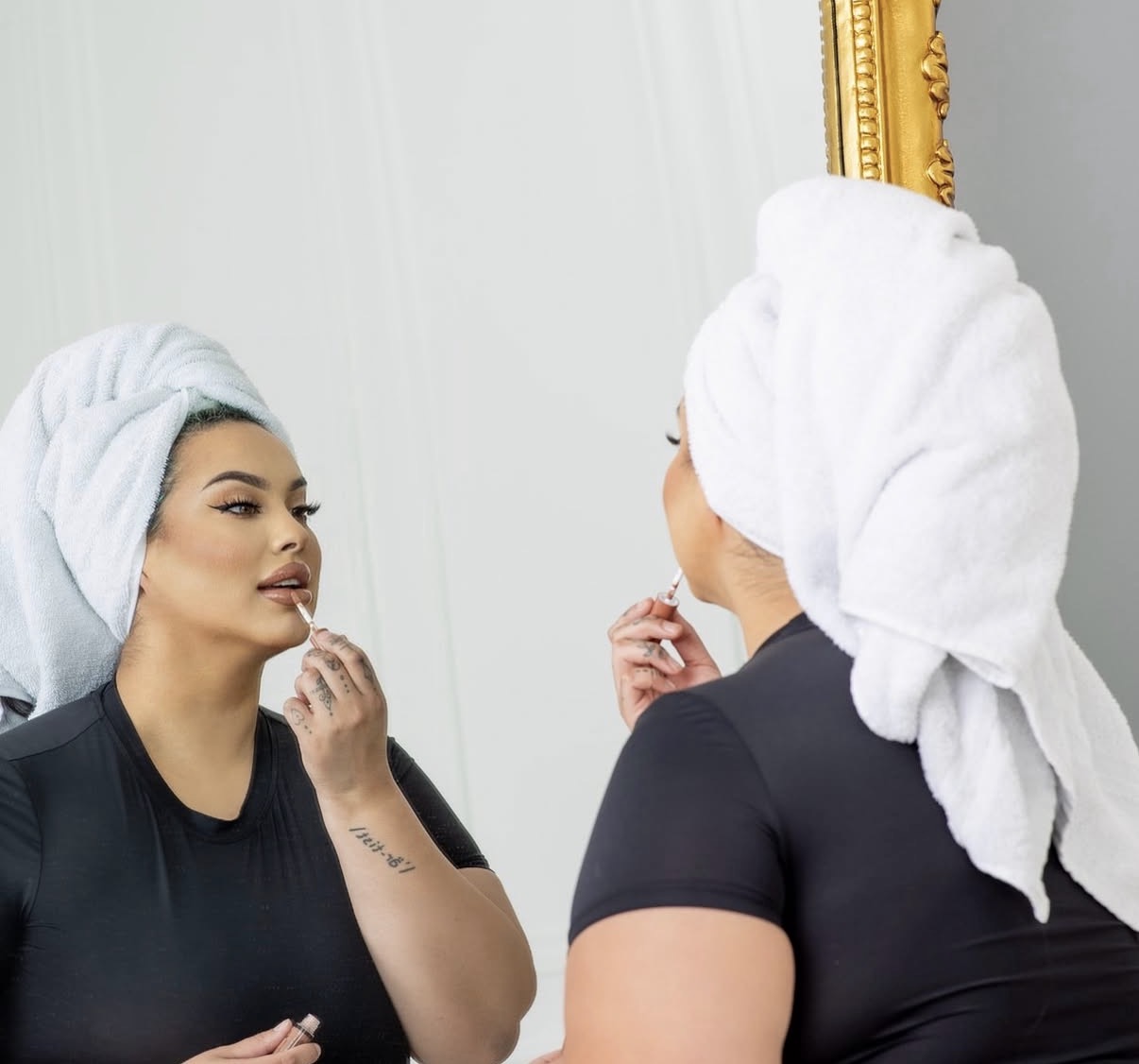 Two women with towels on their heads looking at each other in front of a mirror.