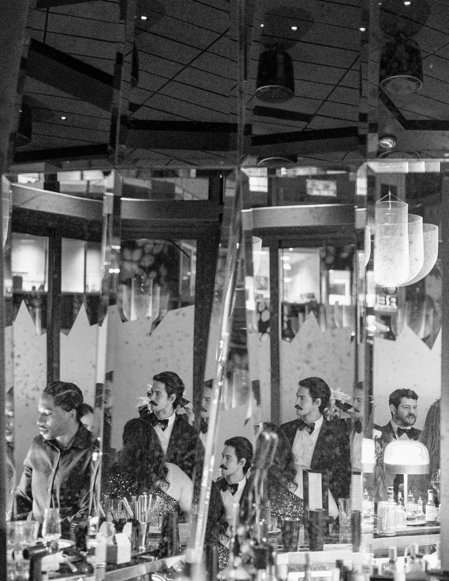 Multiple people standing in a line inside a modern, well-lit indoor space with hanging lights and large windows.