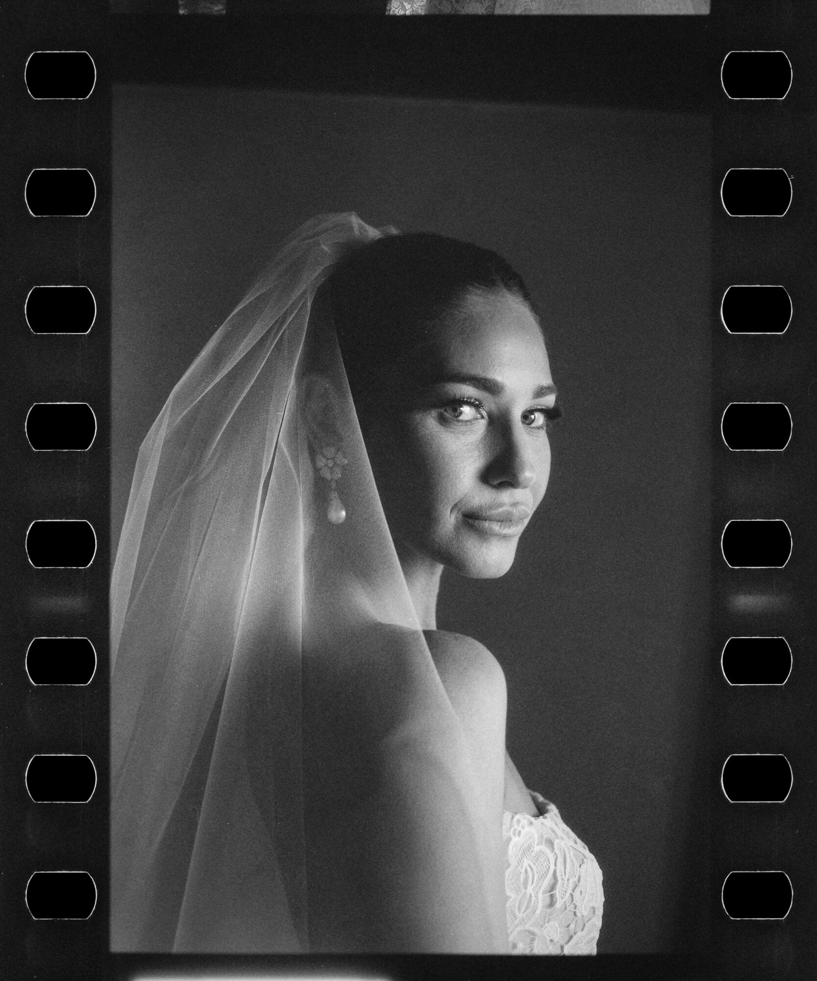 Black and white portrait of a woman with a veil, looking over her shoulder, with a neutral background.