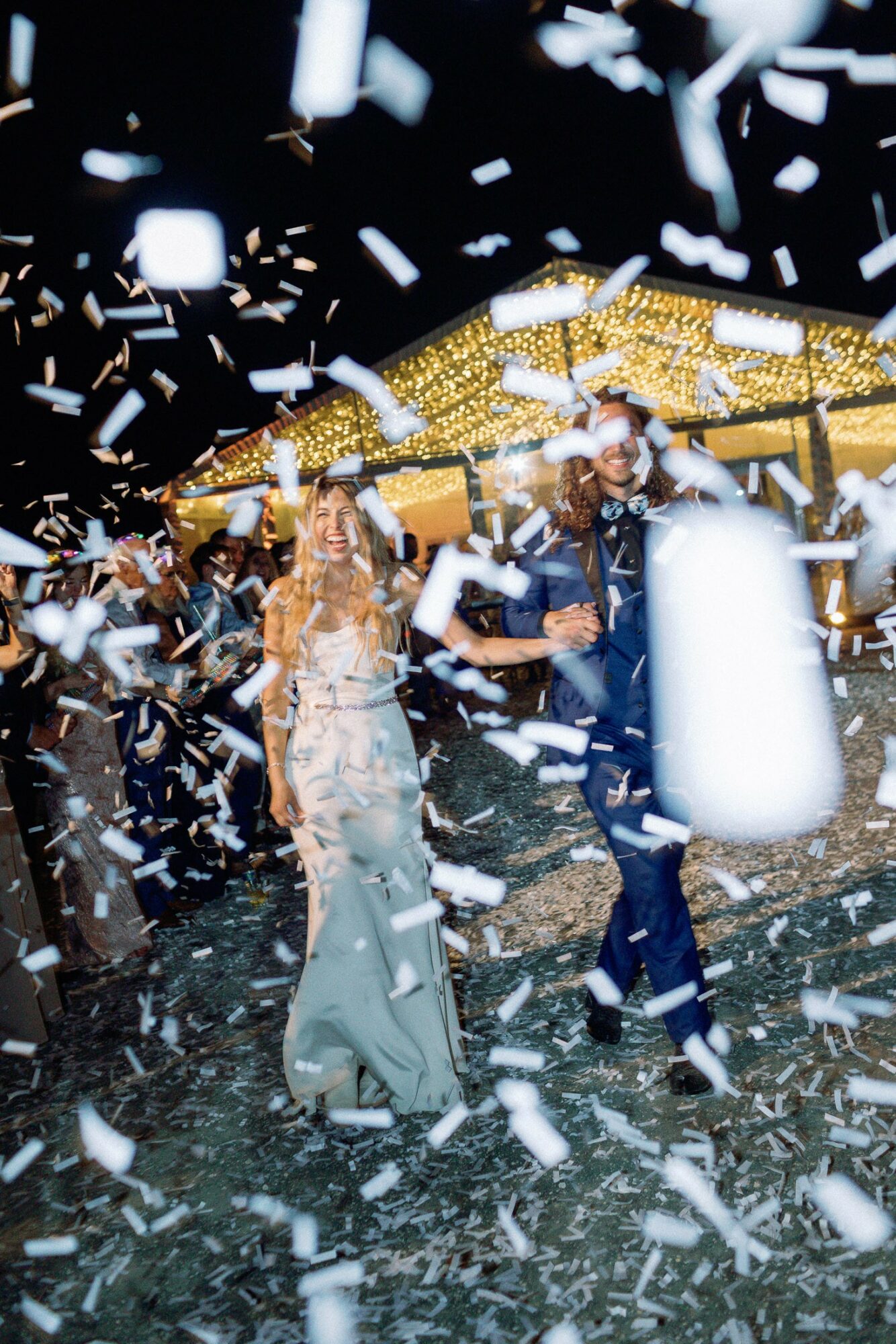 People dancing under a canopy with confetti falling around them at a celebration, with bright lights overhead.