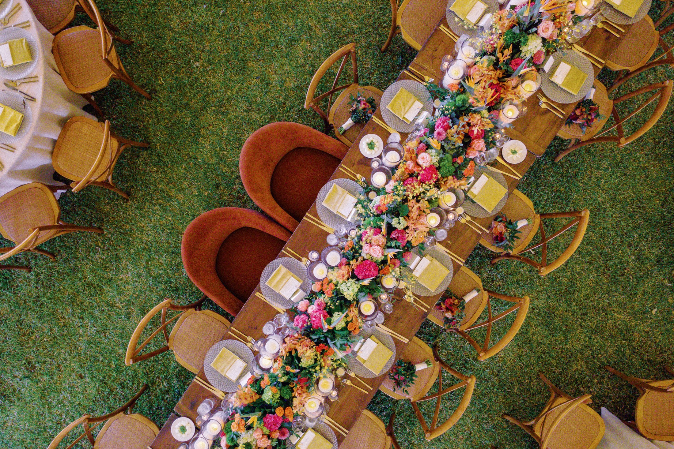 Aerial view of a long banquet table decorated with flowers and surrounded by chairs on grass.