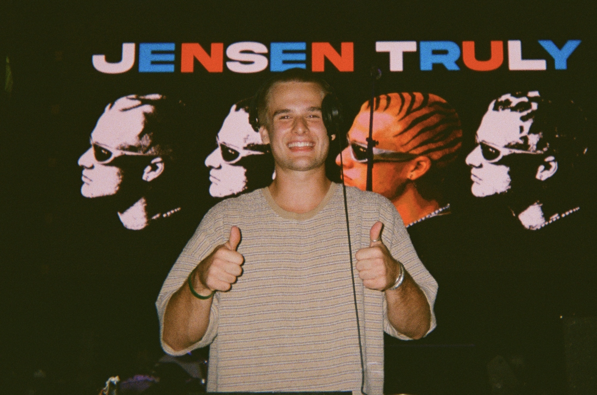 Person smiling and giving two thumbs up in front of a colorful background with silhouettes and text.