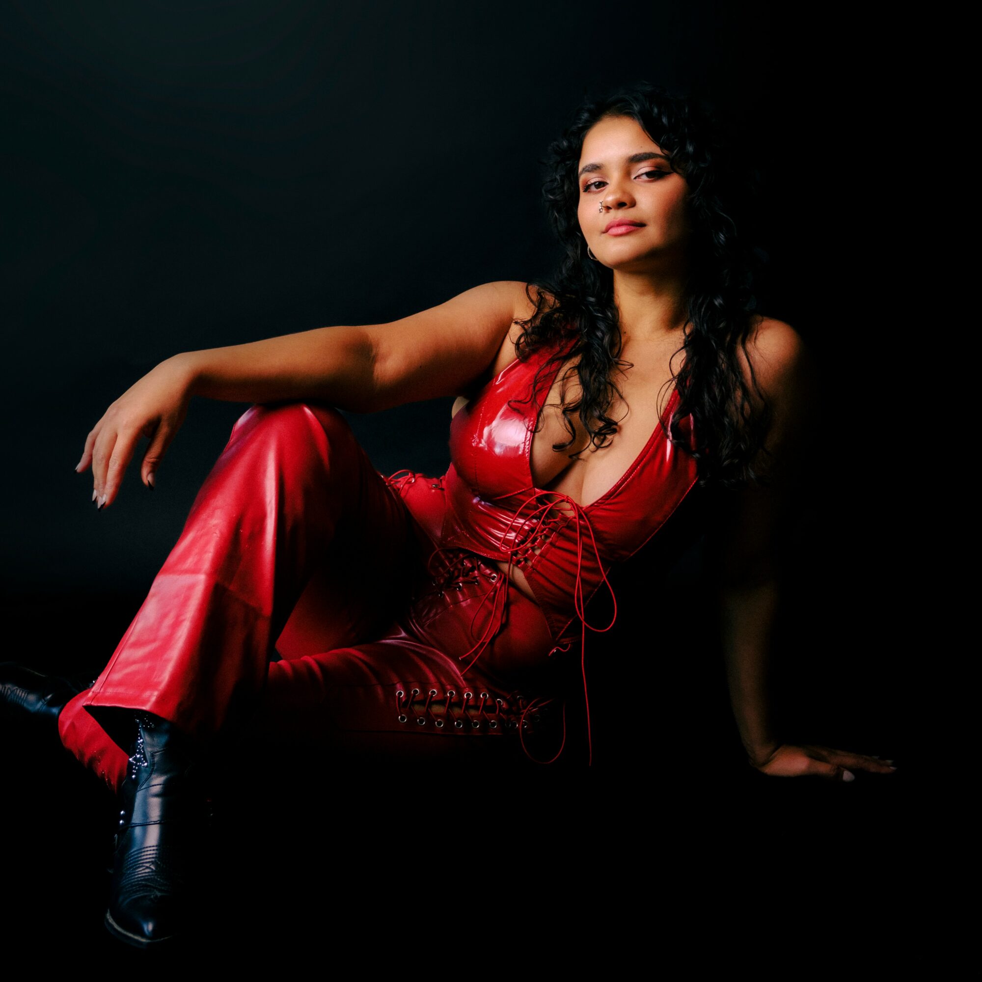 Woman in red outfit sitting against a dark background, looking at the camera with a confident expression.