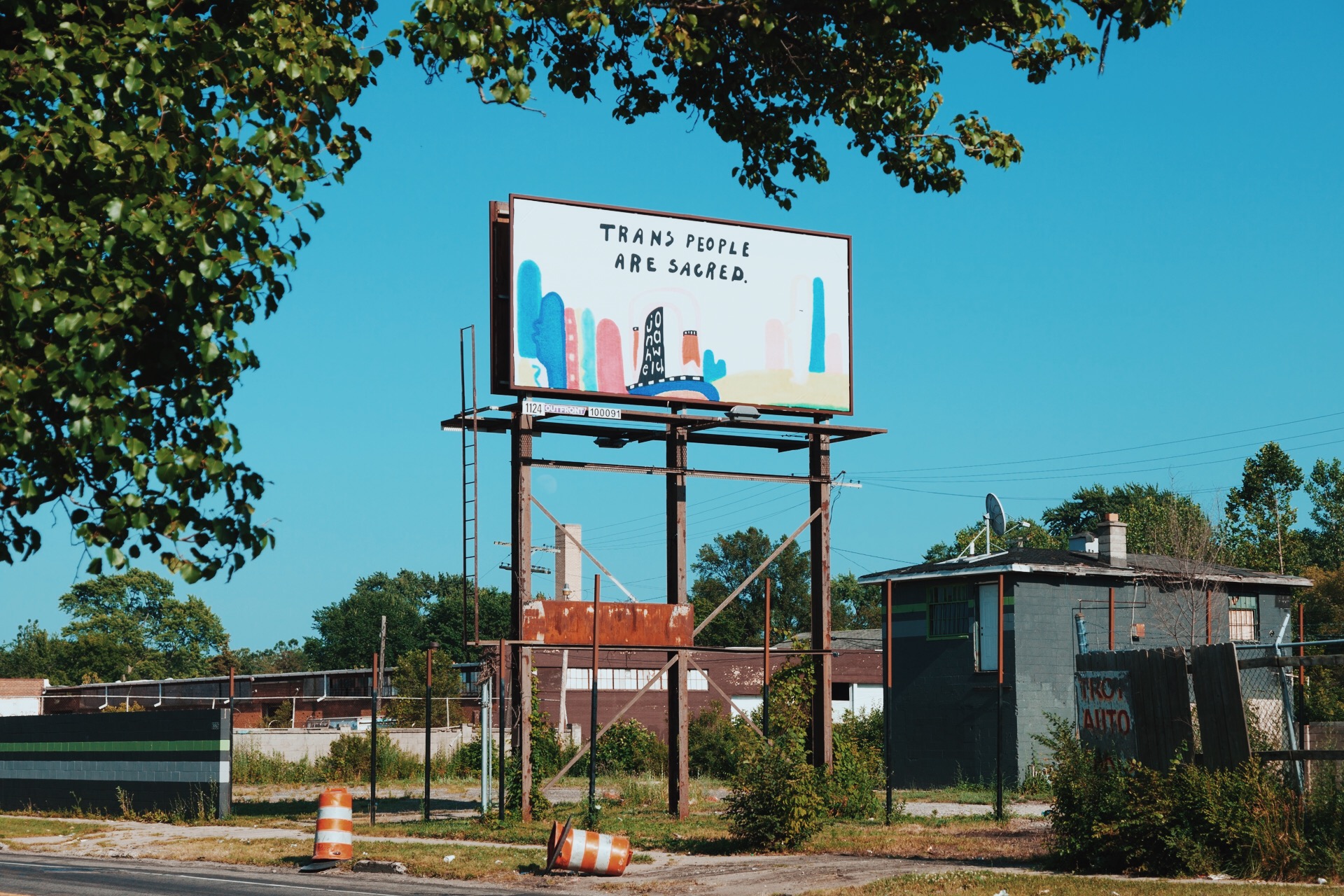 Billboard advertising Tranz People Art Gallery, with trees and buildings in the background.