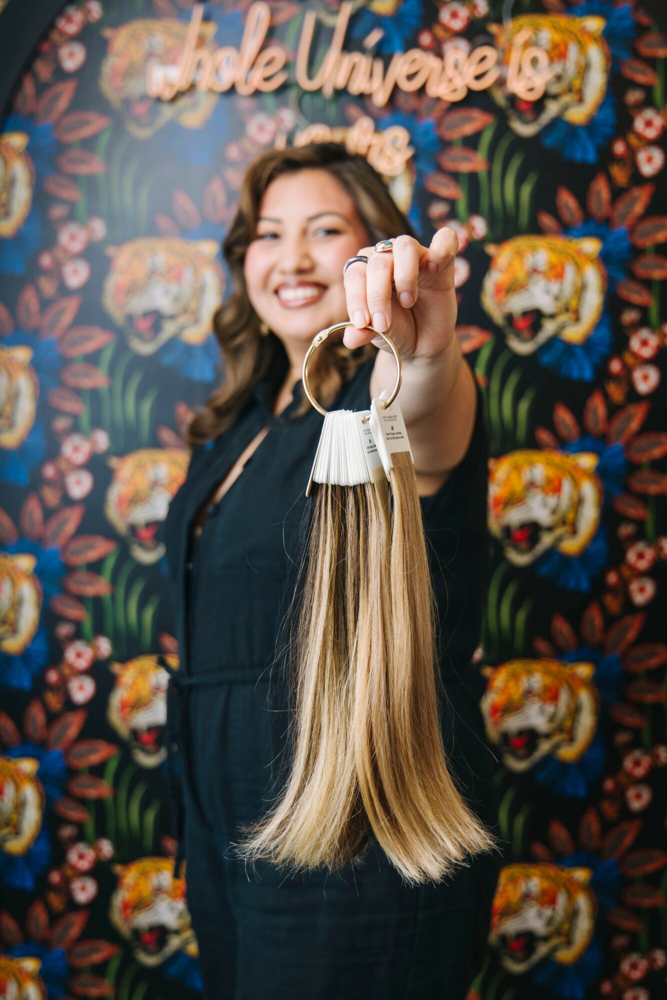Smiling woman holding a bundle of long blonde hair extensions in front of a floral background with text.