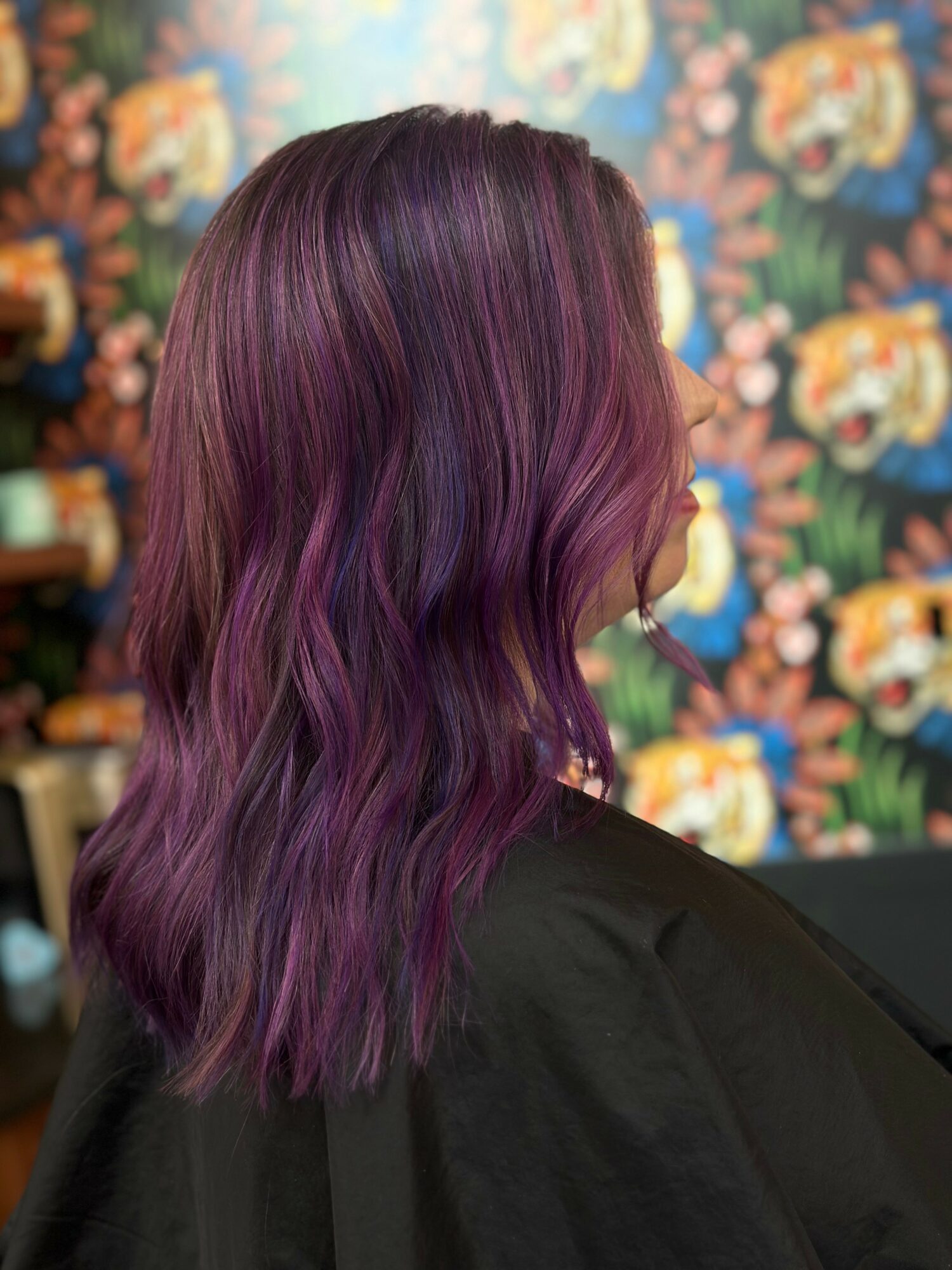 Side view of a person with wavy, purple and pink ombre hair against a floral background.