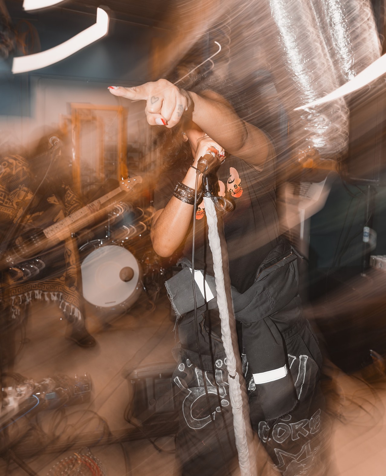 Person pointing with finger, holding microphone, in a lively indoor setting with musical instruments, motion blur present.