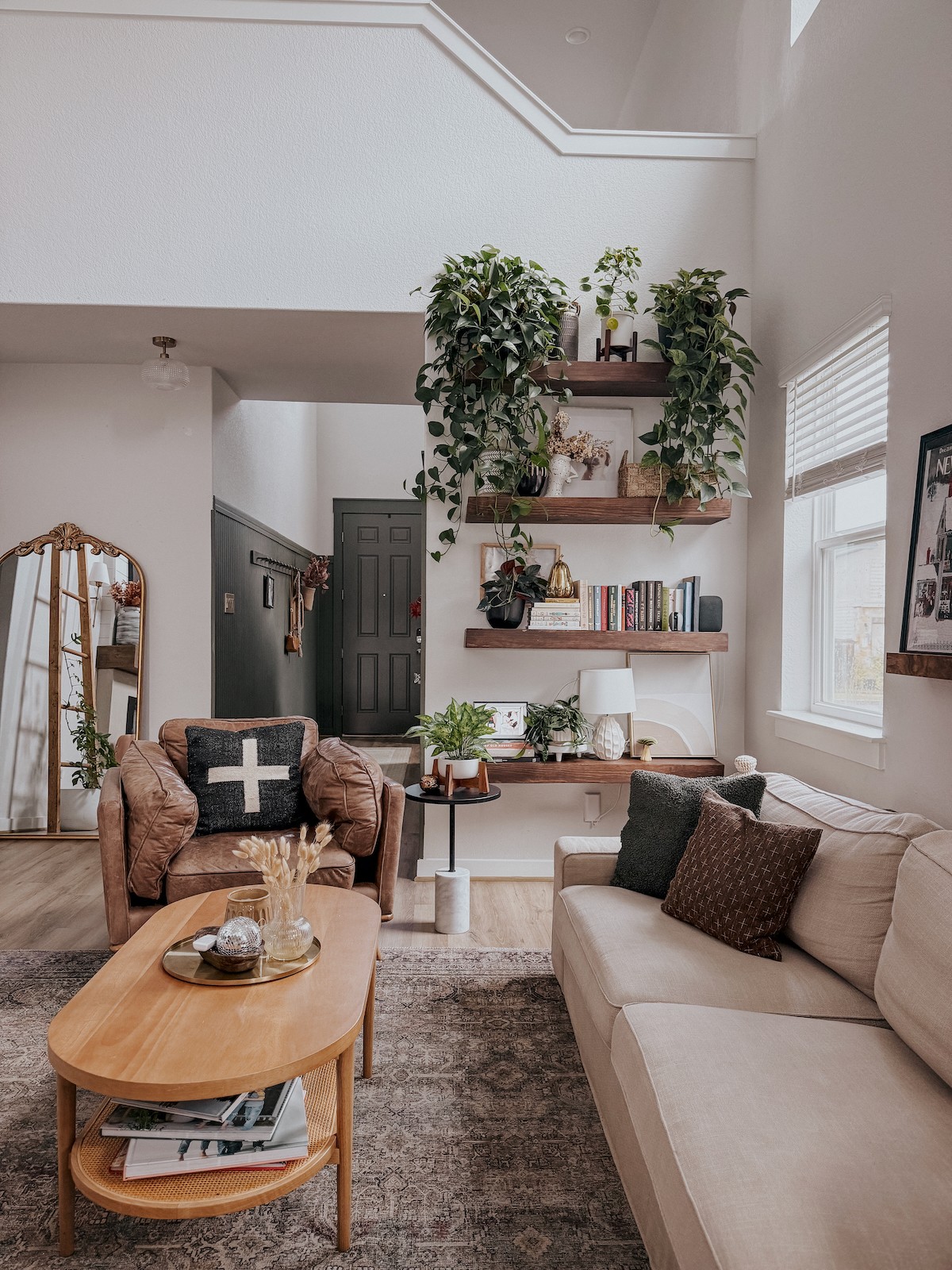 Living room with beige and brown sofas, wooden coffee table, and wall shelves with plants and books.