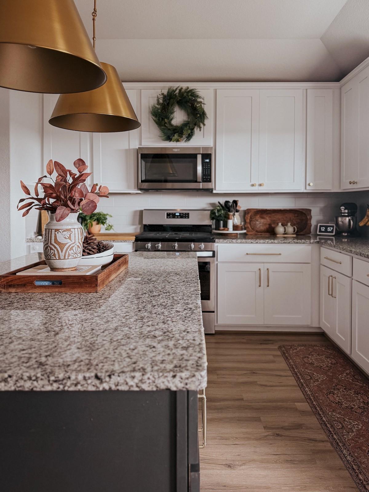 Kitchen with white cabinets, granite countertop, microwave, stove, and decorative wreath, flowers, and kitchen items on the counter.
