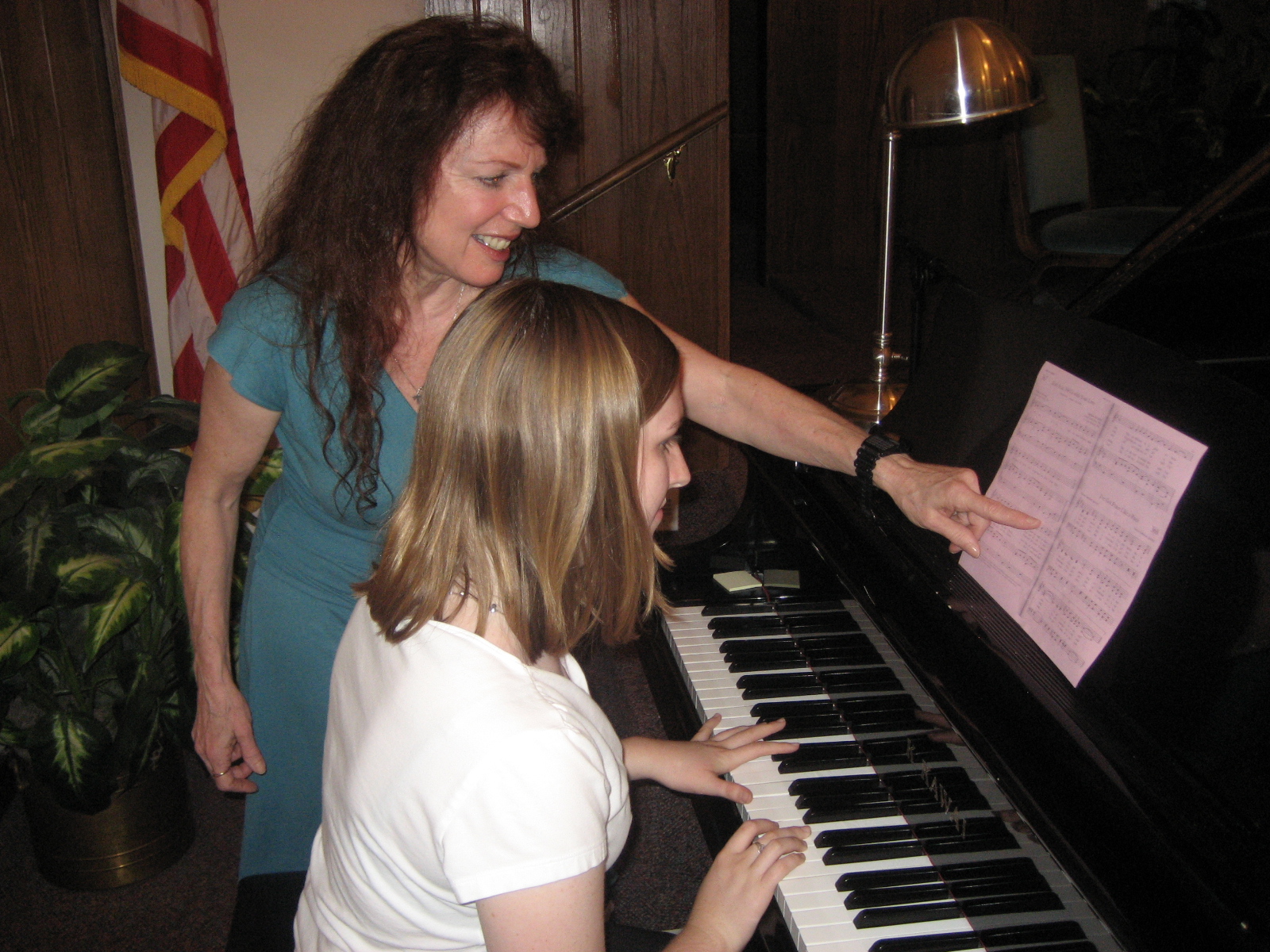 Two women, one older and one younger, are at a piano with sheet music, smiling and engaging in a music lesson.