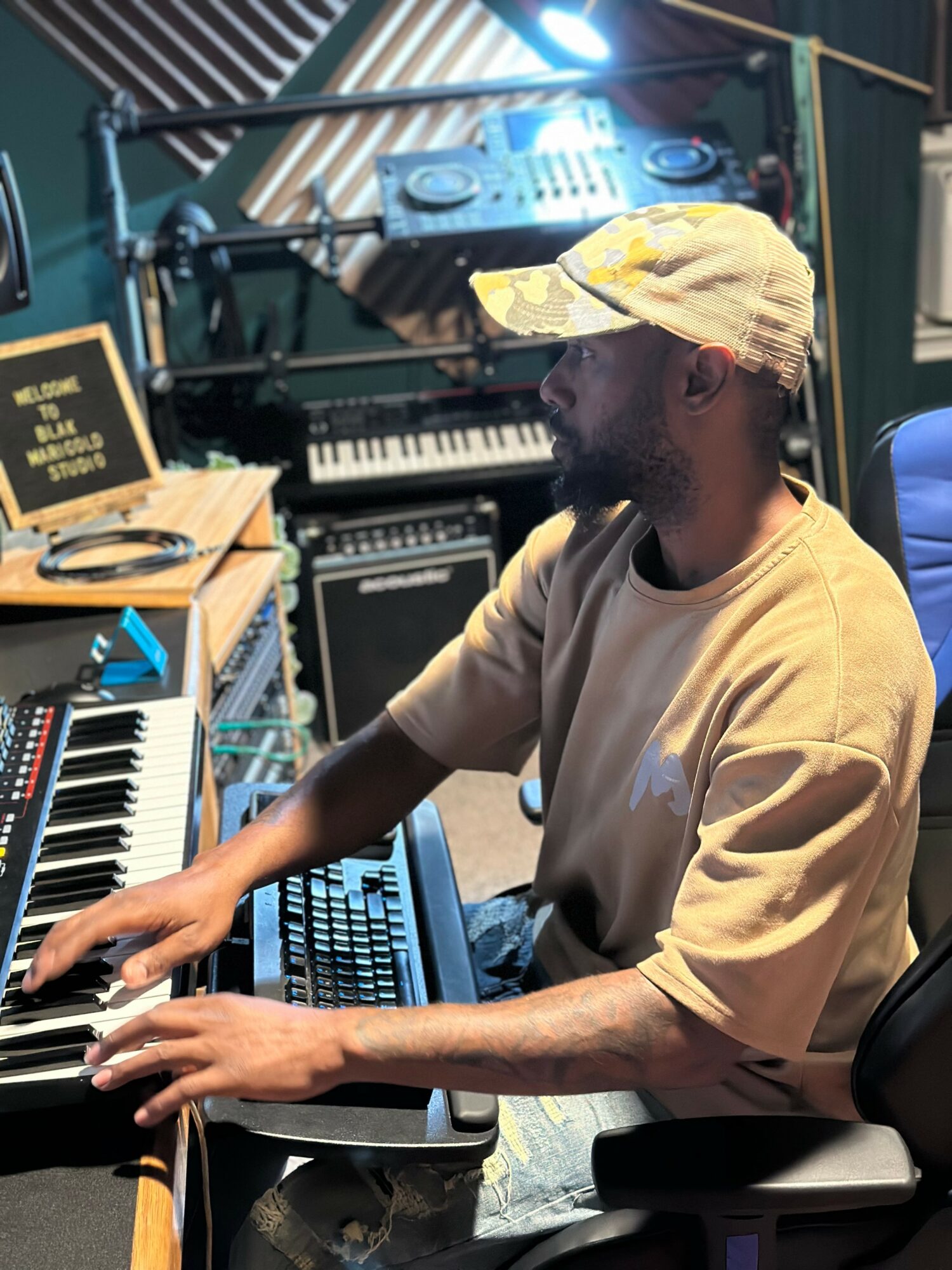 Person playing keyboard in a music studio with equipment and a DJ controller in the background.