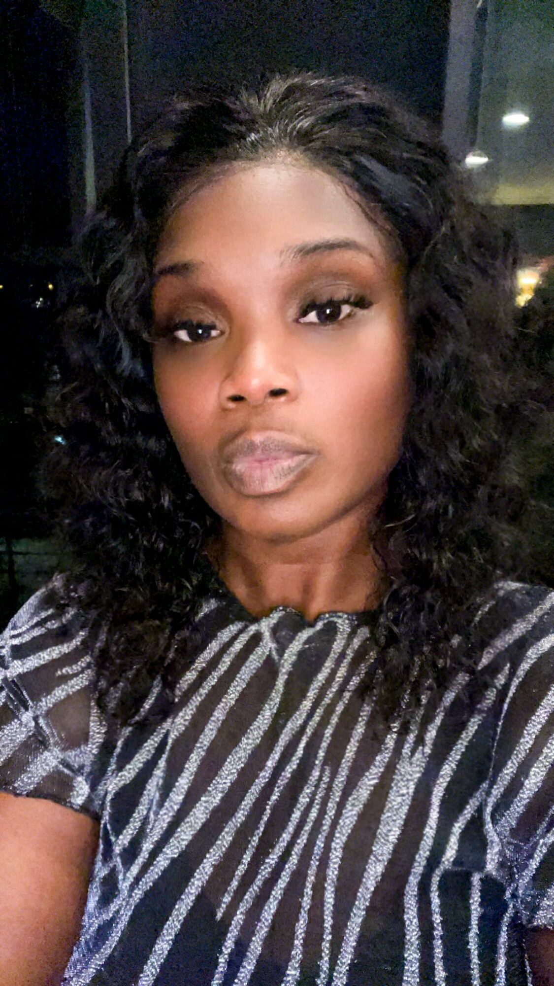 Woman with curly hair and makeup, wearing a striped top, looking at the camera.