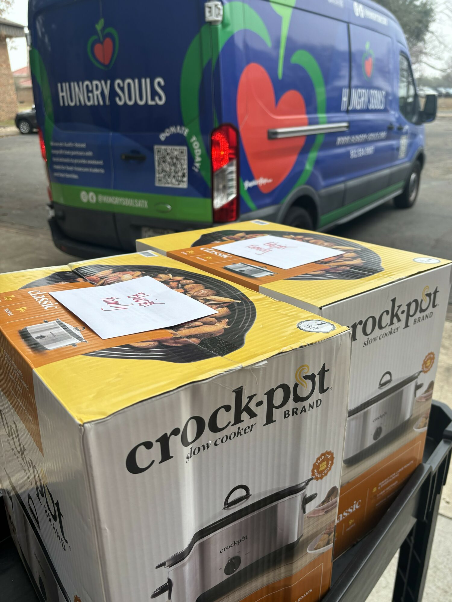 A boxed Crock-Pot slow cooker on a shopping cart, with a colorful van in the background featuring a heart and the words 'Hungry Souls'.