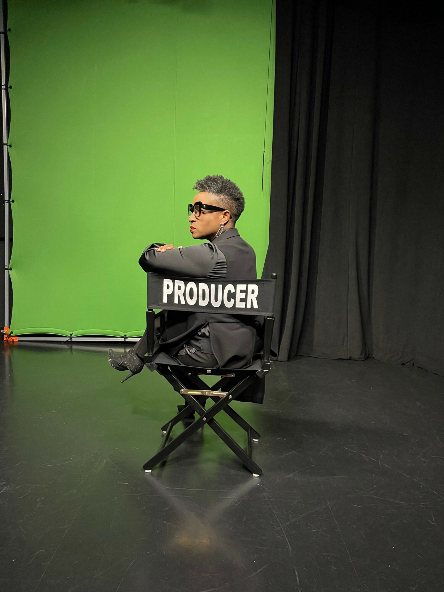 Person sitting on a chair labeled 'PRODUCER' in front of a green screen, in a studio setting.