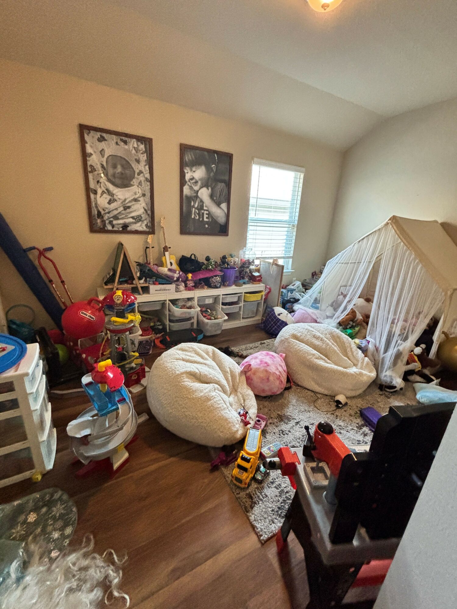 Room with toys, stuffed animals, and furniture, viewed from a tilted angle. Window and wall art visible.
