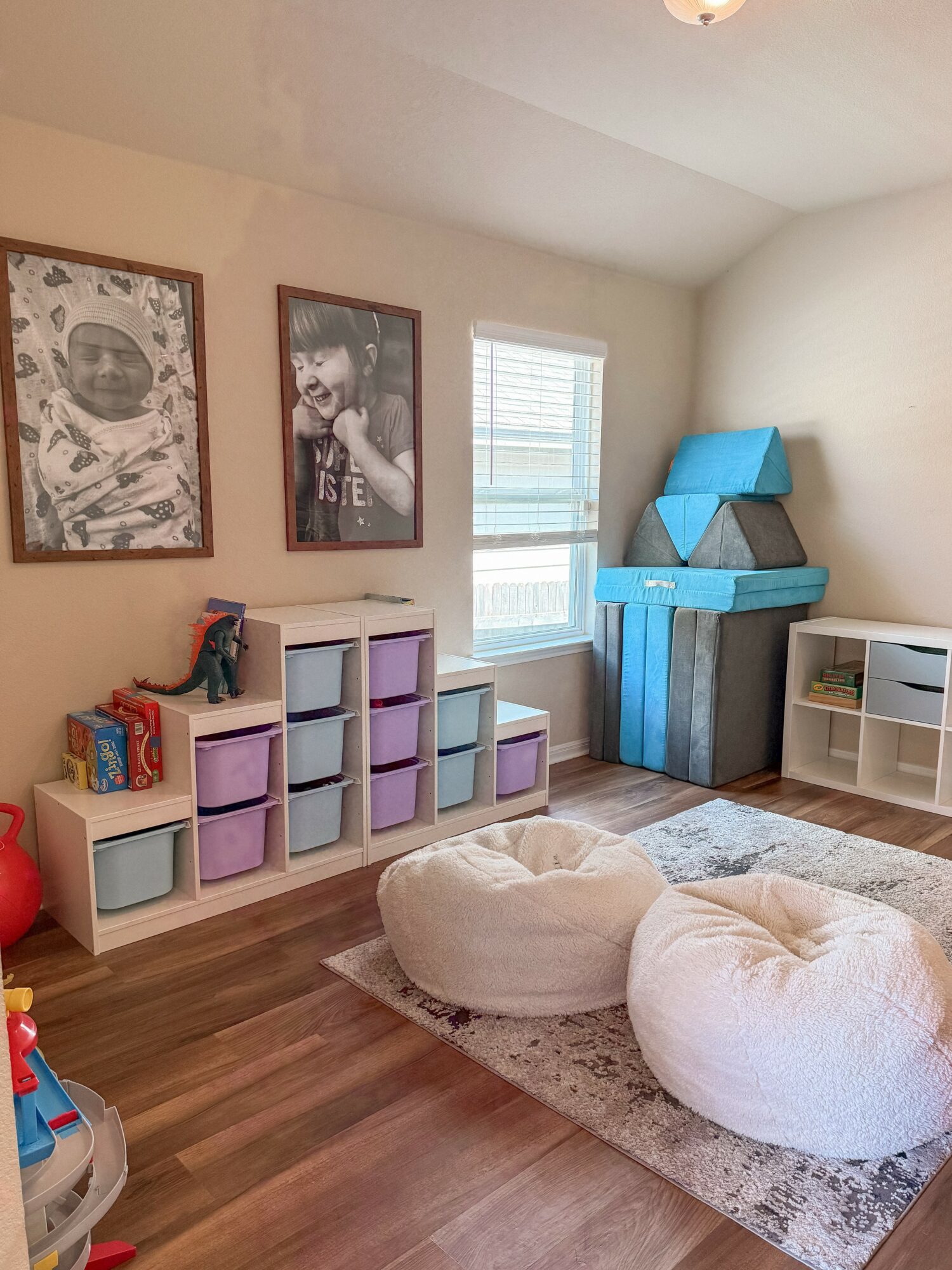Child's playroom with storage bins, bean bag chairs, and wall art, illuminated by natural light from a window.