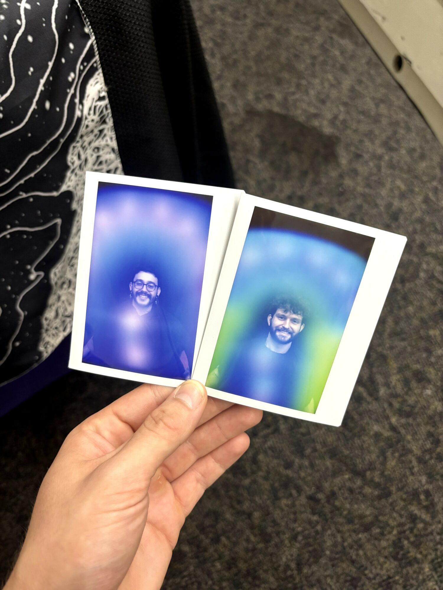Person holding two photo booth pictures of a smiling man with glasses, one with a blue background, the other with a green background.