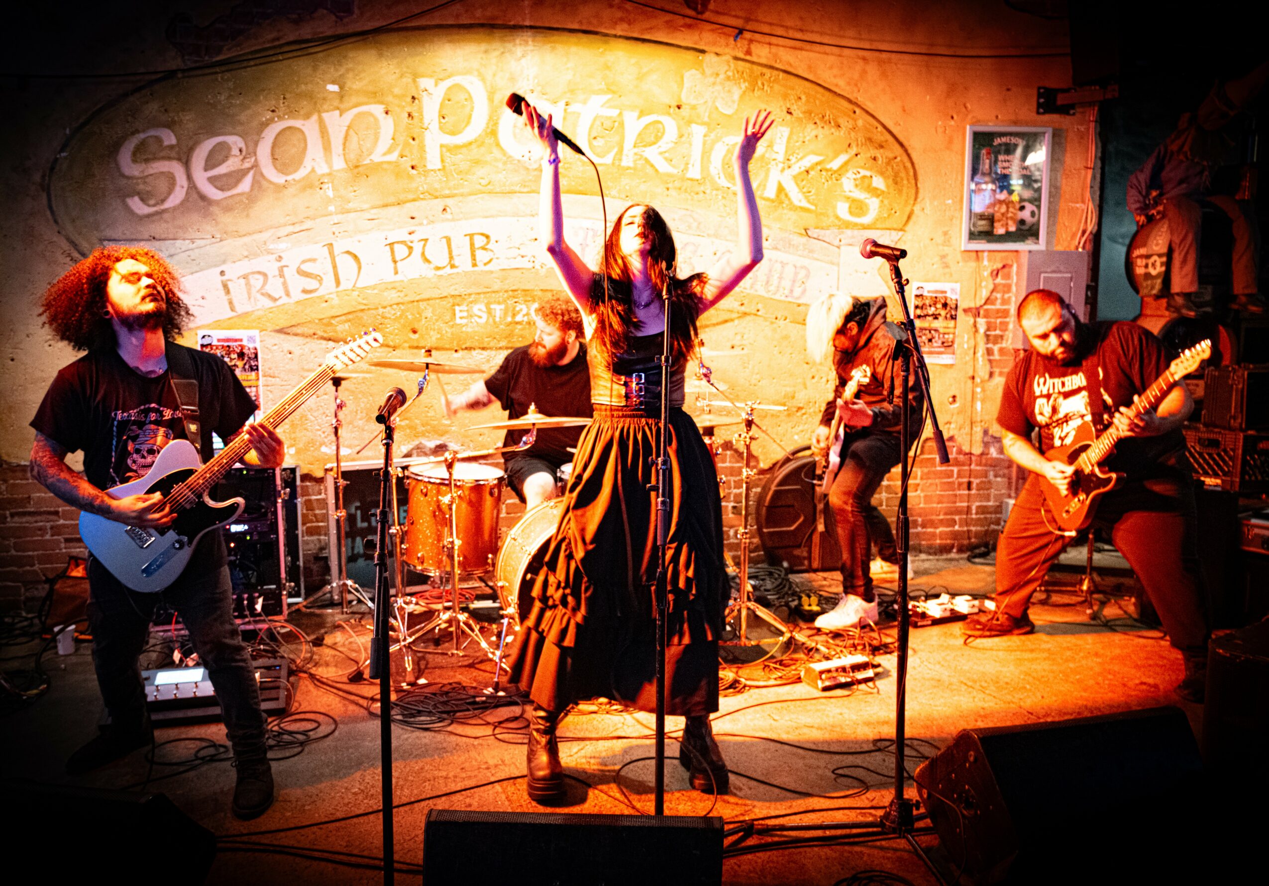 Band performing on stage with five musicians, a woman singing, and a colorful backdrop reading 'Sean Patrick's Irish Pub'.