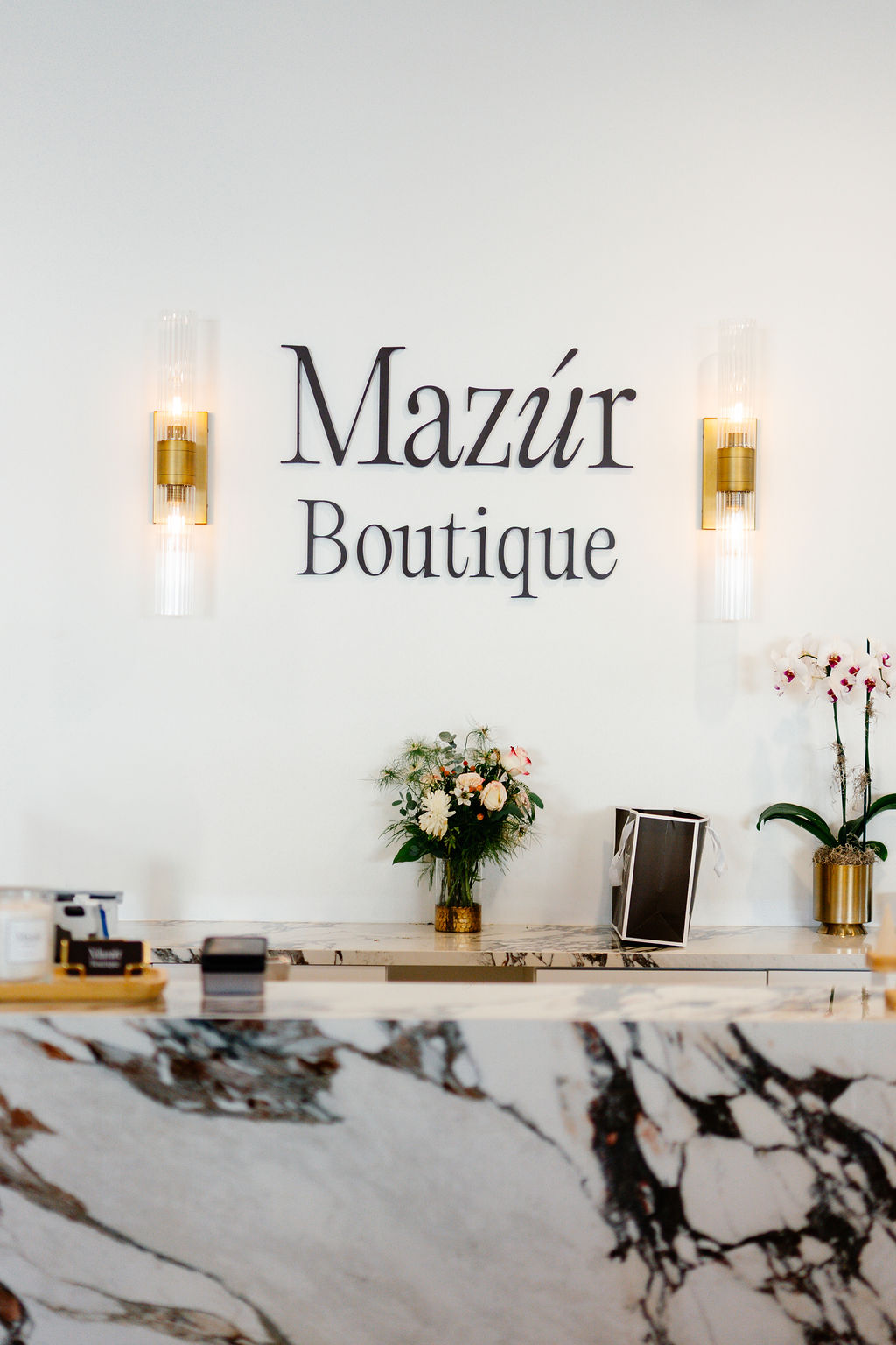 Boutique reception area with a marble counter, floral arrangement, and the sign 'Mazúr Boutique' on the wall.
