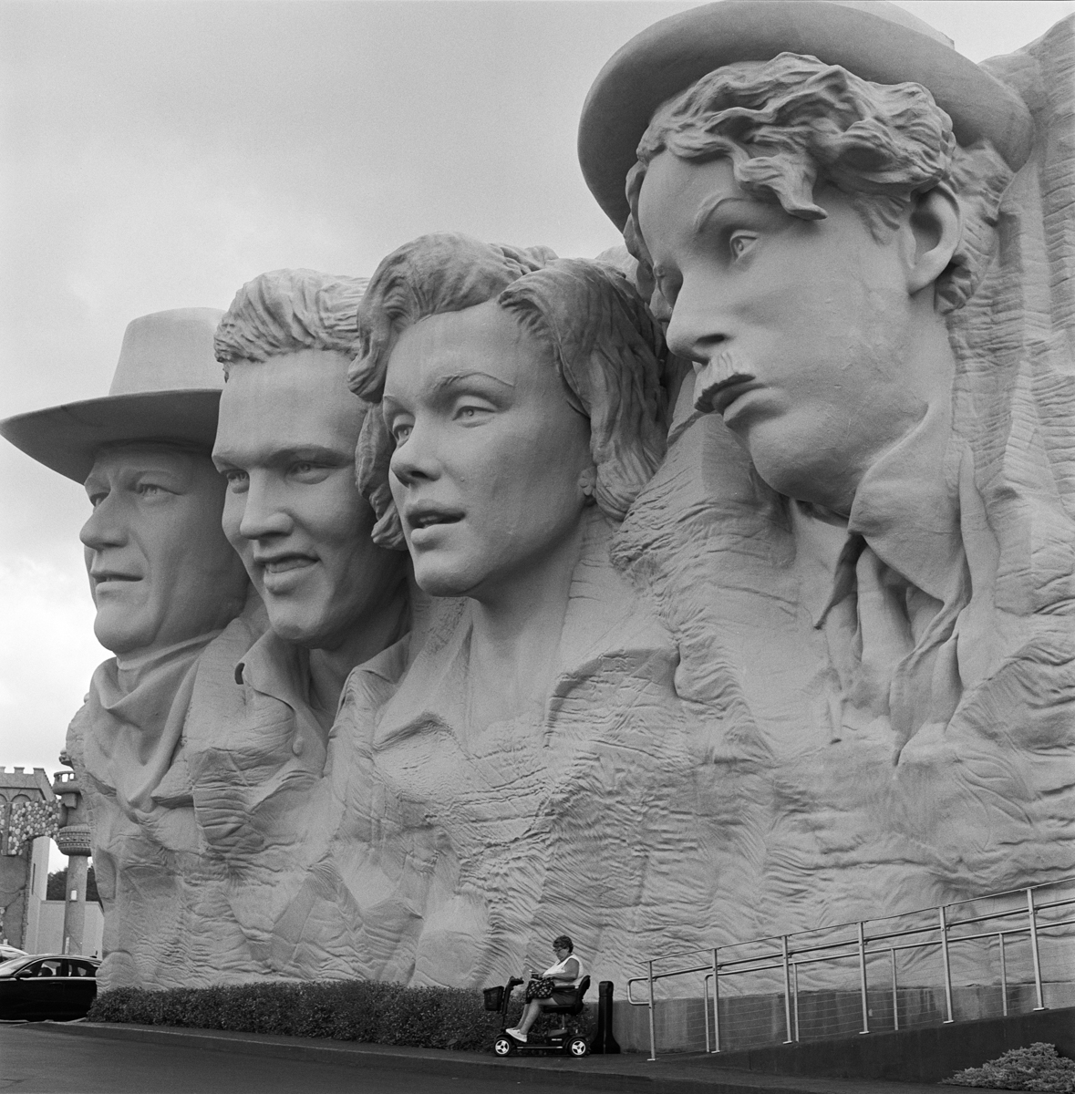 Four large stone sculptures of people's heads and shoulders, with a person sitting on a bench below, in front of the monument.