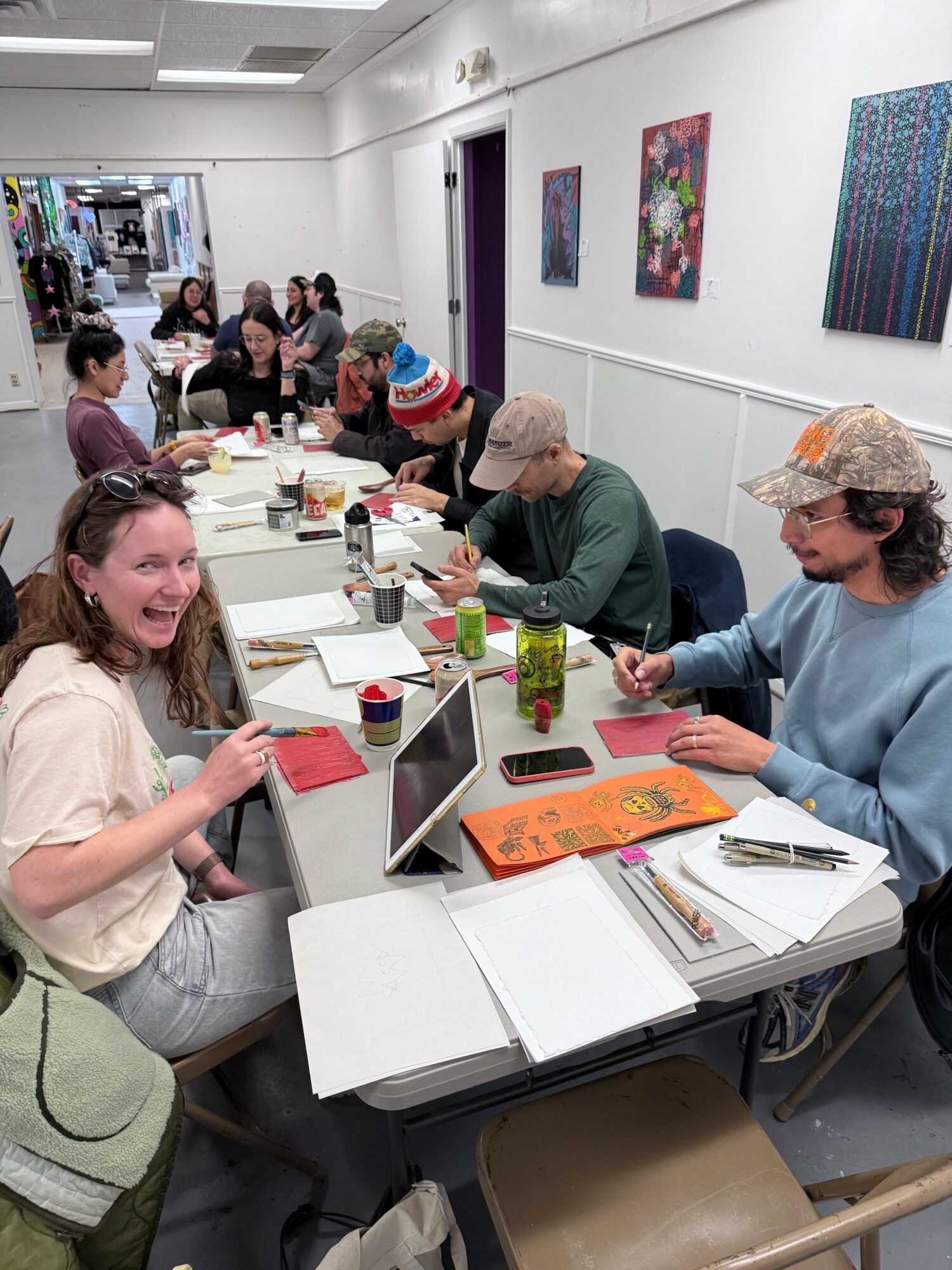 Group of people sitting around a table in a room with white walls and colorful artwork, engaging in a meeting or workshop.