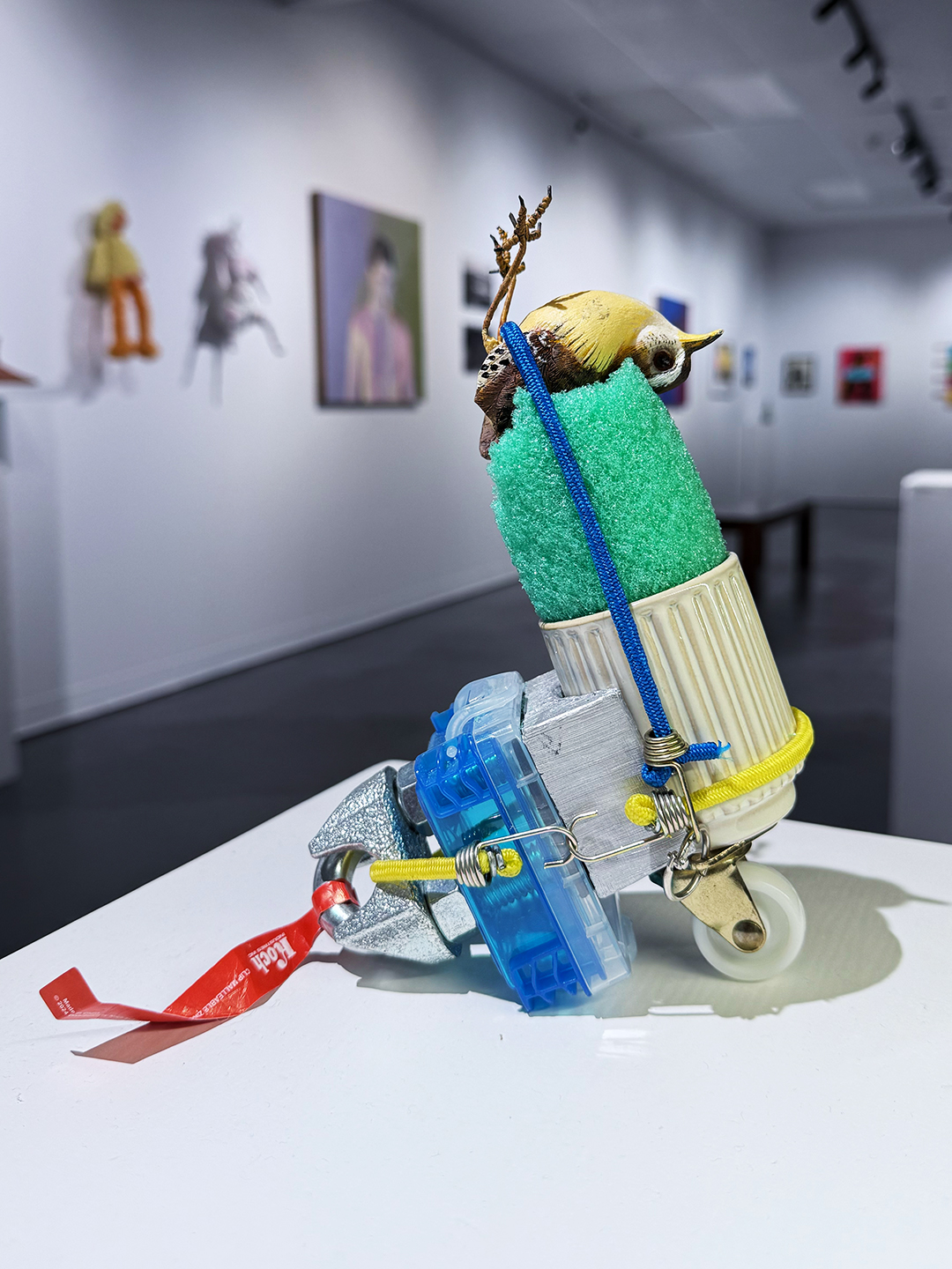 Mixed media sculpture of a fish with antlers, glasses, and a snorkel, displayed on a white table in an art gallery.