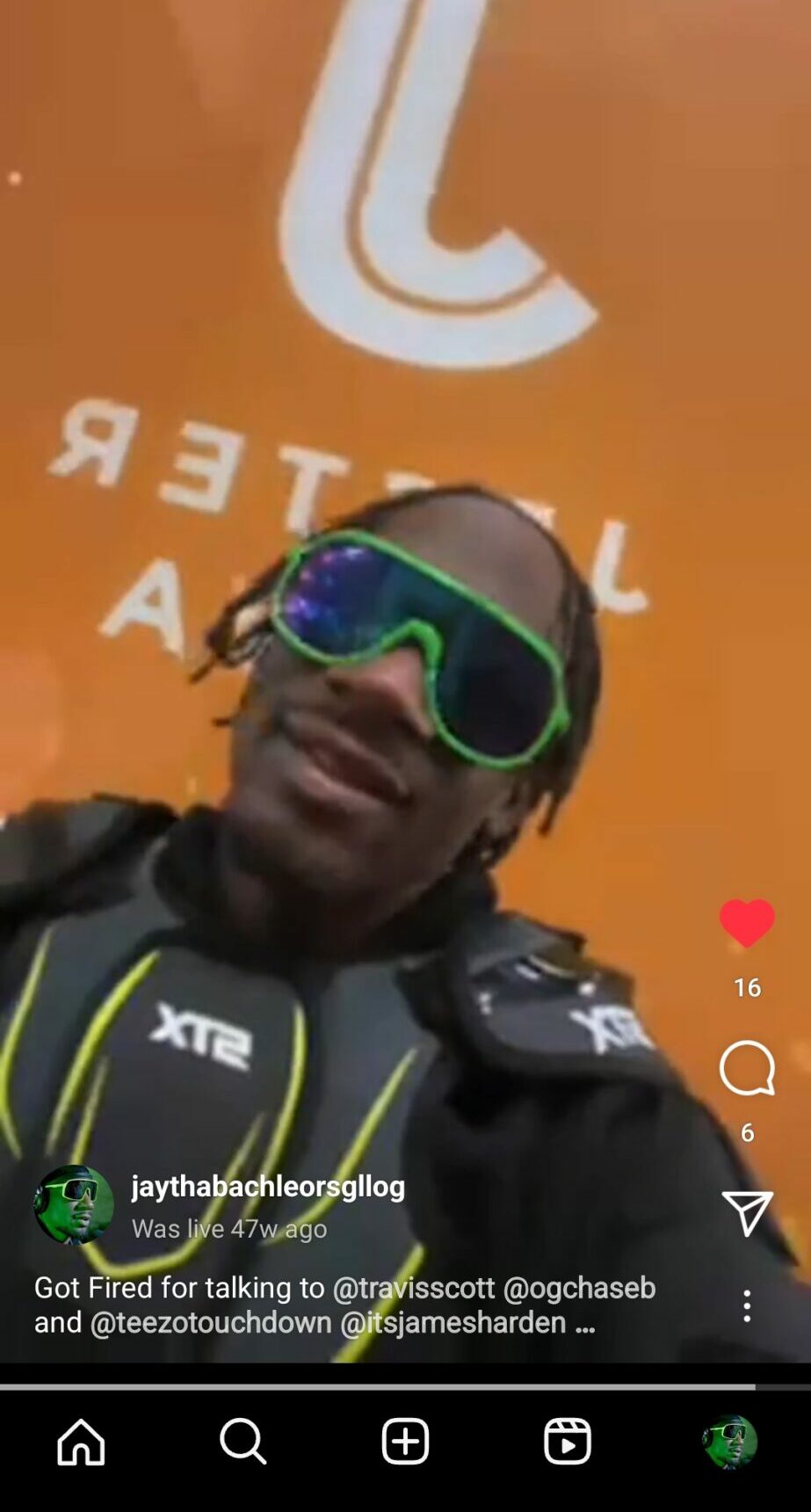 Person wearing sunglasses with a colorful frame, dark clothing, and a backpack, standing in front of an orange wall with white text.