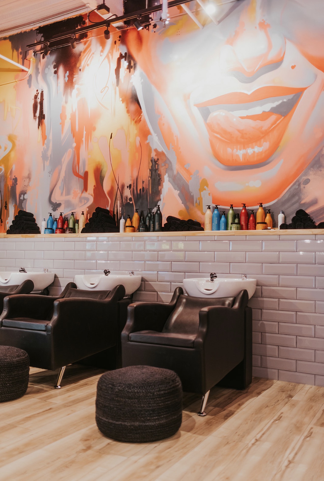 Salon with three black chairs, white sinks, and a large mural of a smiling woman's face on the wall.