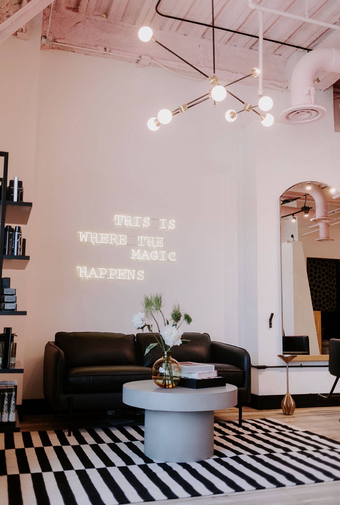 Living room with black sofa, round white coffee table, striped rug, and wall projection with text, modern lighting, and decor.