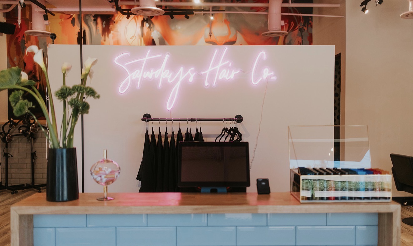 Counter with a vase of flowers, a small glass object, a tablet, and a display case, with a neon sign in the background.
