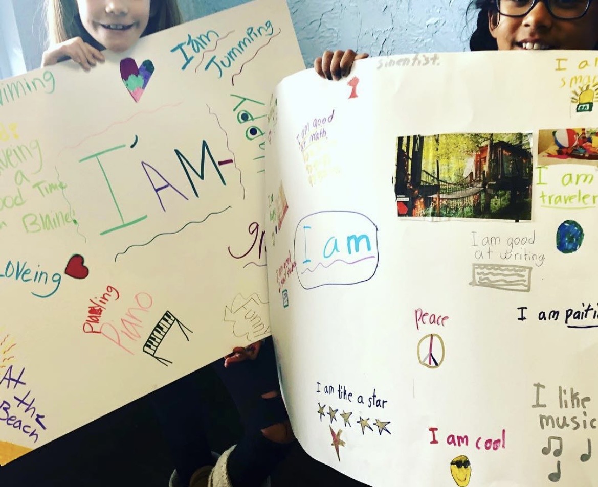 Two children hold colorful posters with drawings and writings, smiling and showing their artwork.