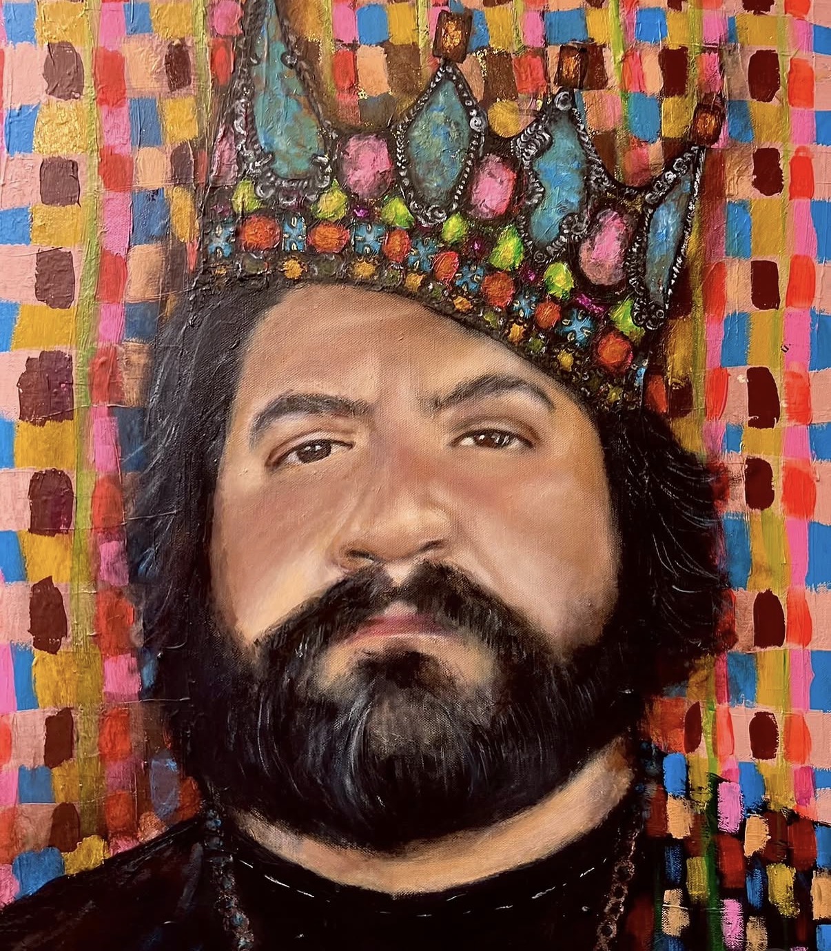 Portrait of a man with a beard wearing a colorful crown, against a multicolored checkered background.