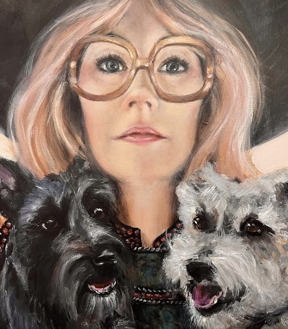 Woman with pink hair and large glasses, flanked by two dogs, one black and one gray, both with open mouths.