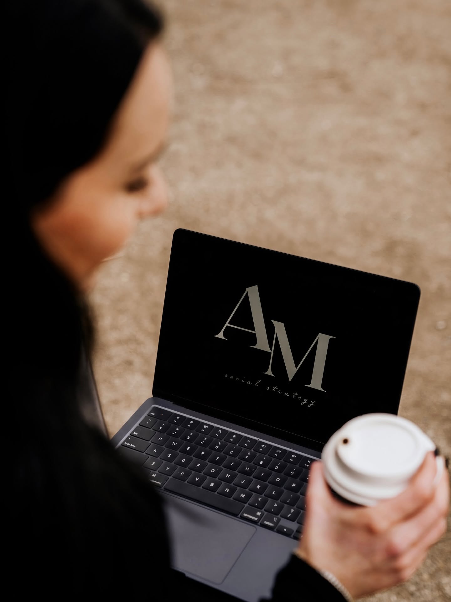 Person holding a coffee cup looking at a laptop with a black screen displaying 'AM' in white letters.