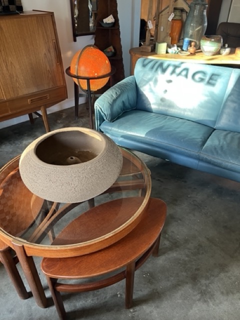 Living room with a blue sofa, wooden table, and various decorative items, including a lamp and bottles.