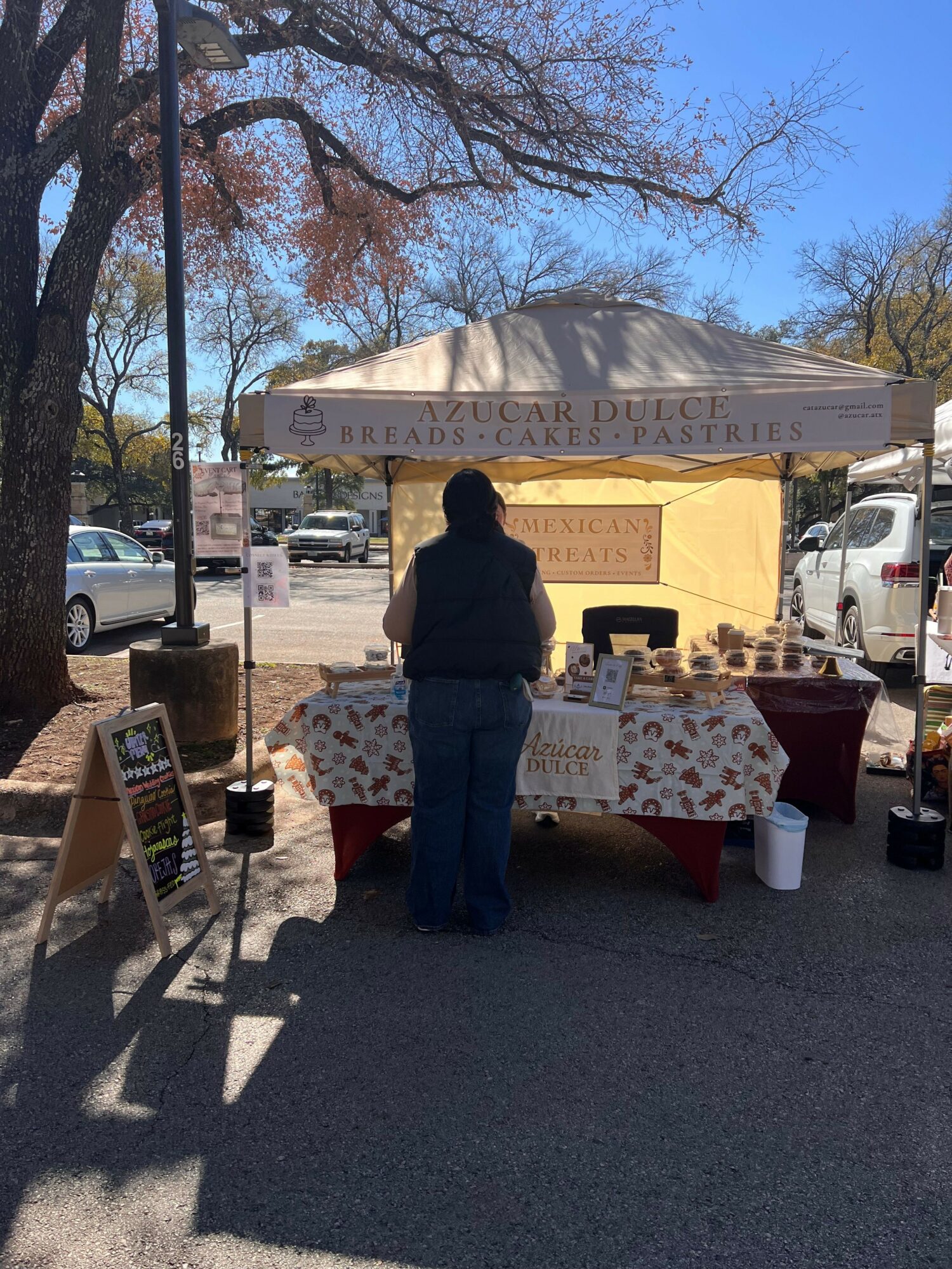 Person standing near a booth with a canopy, table, and various items outdoors on a sunny day.