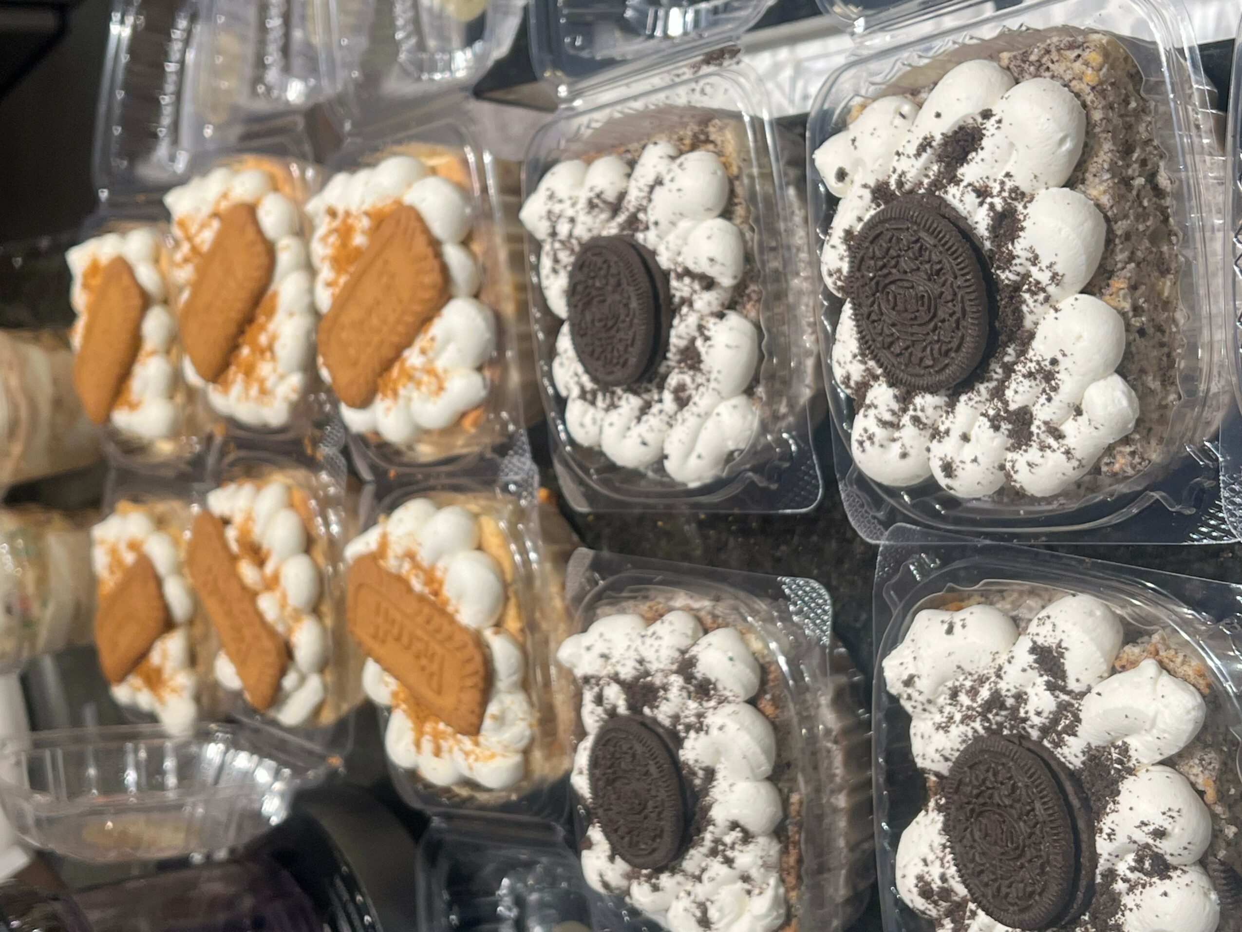 Multiple dessert cups with whipped cream, Oreo cookies, and cookies on top, arranged in rows.