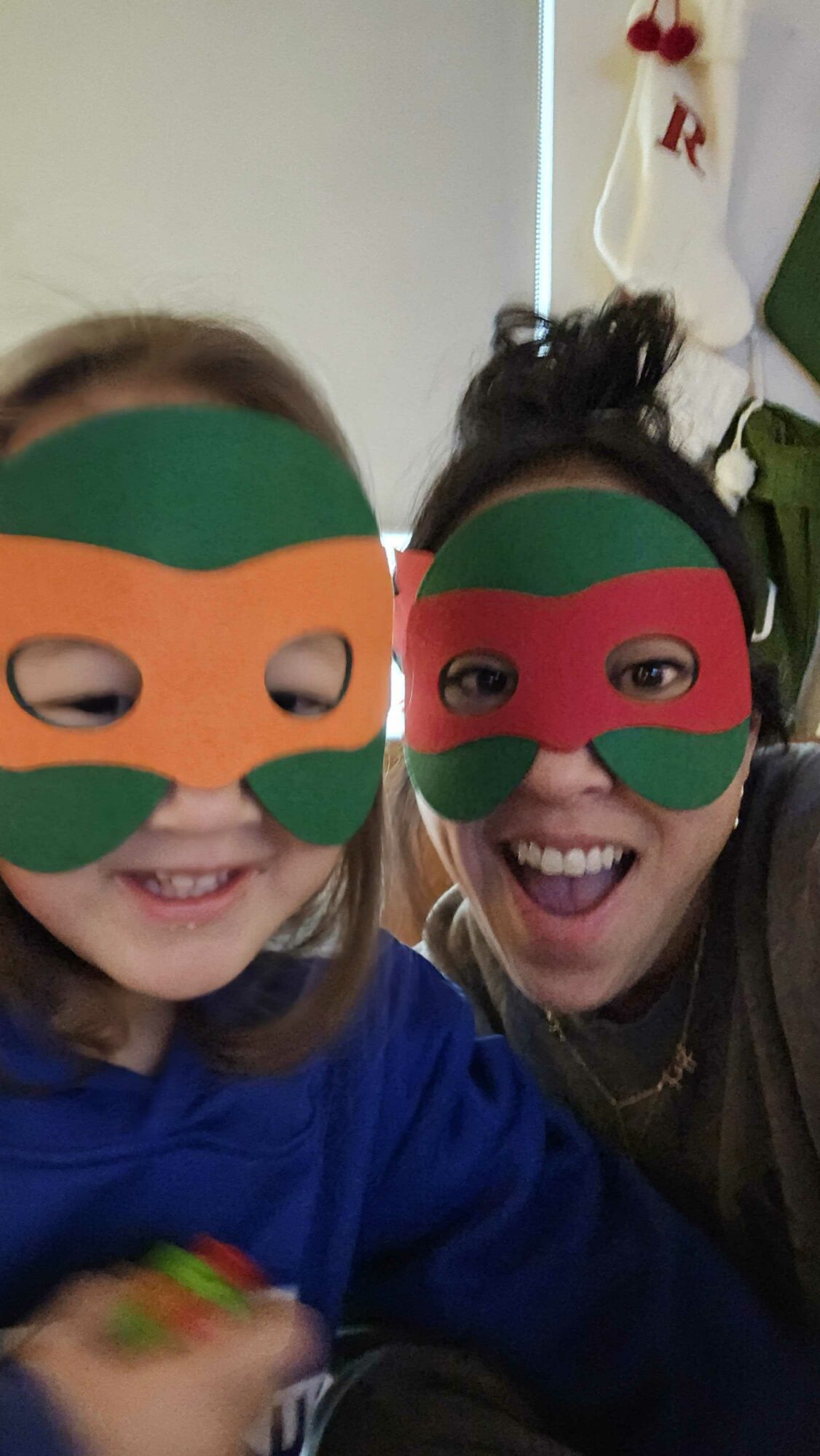 Two people wearing colorful superhero masks smiling for a photo indoors.