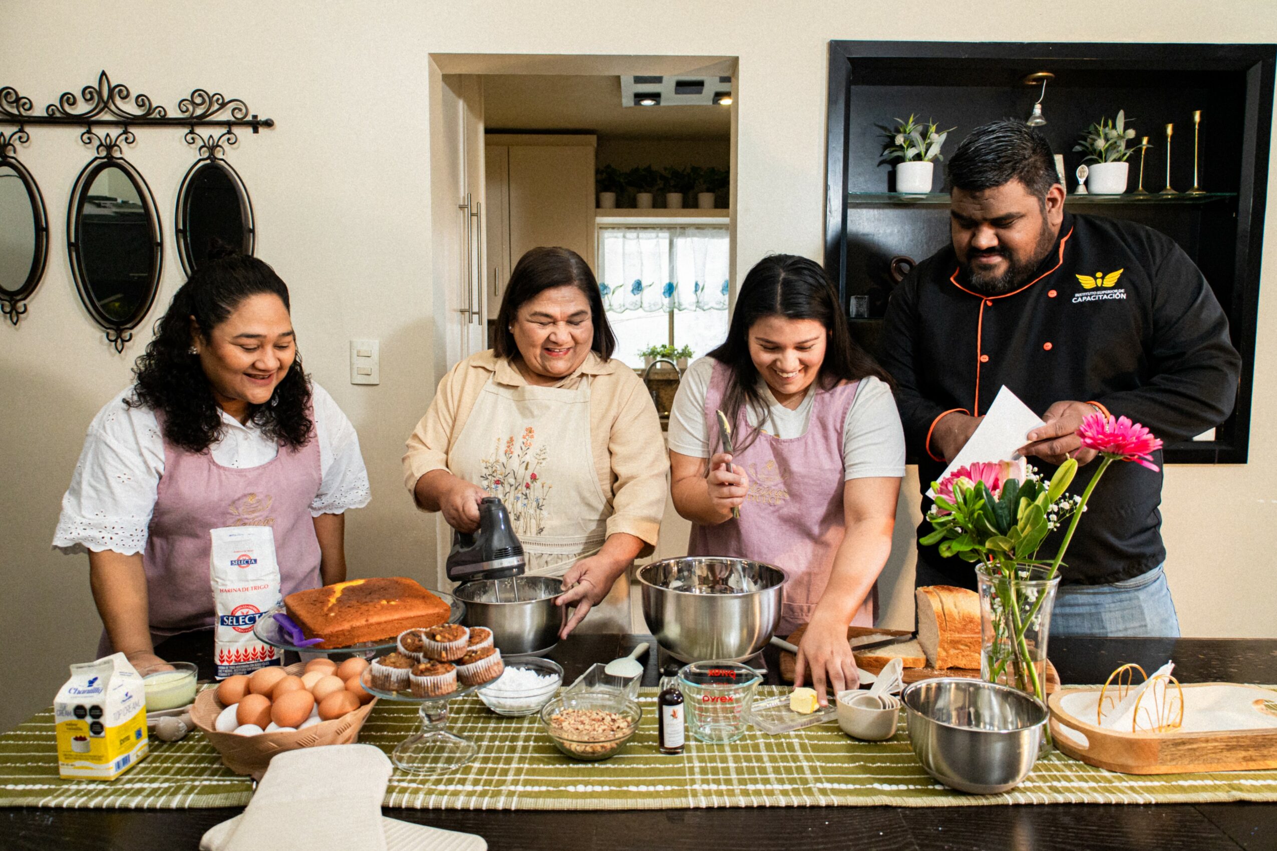 Four people in a kitchen preparing food together, with eggs, bread, and baking ingredients on the counter.