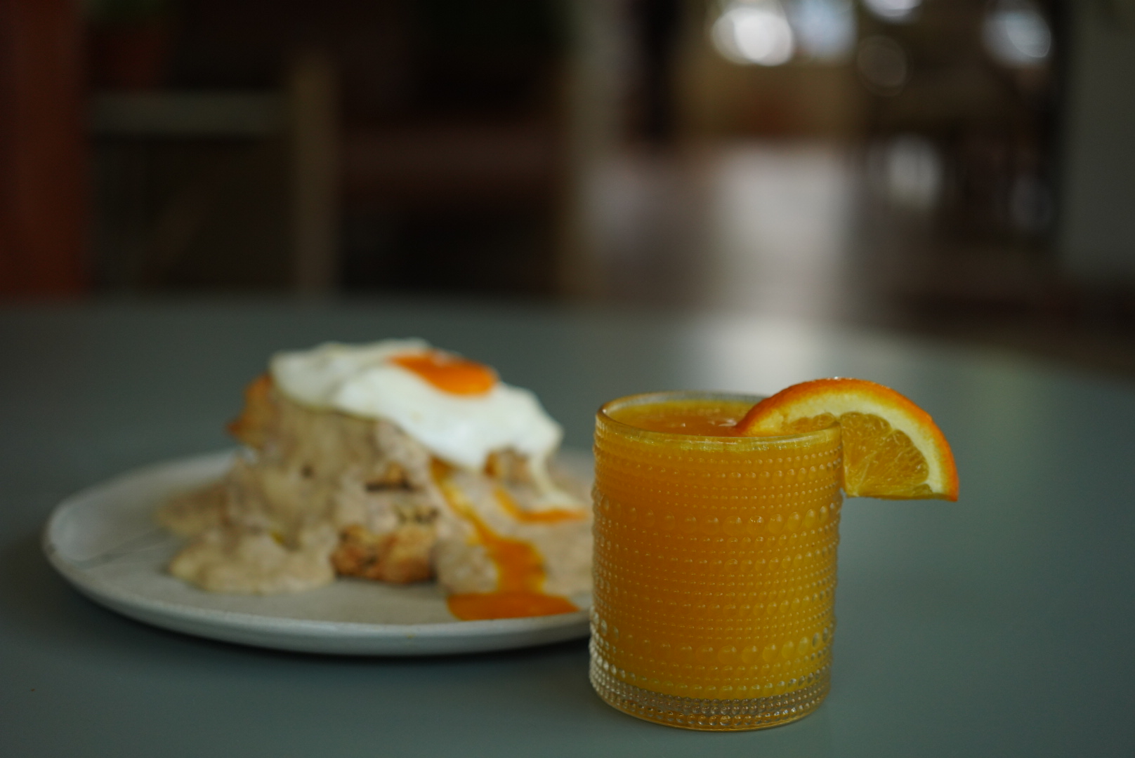 A plate with rice, fried egg, and sauce, alongside a glass of orange juice with an orange wedge, on a table.