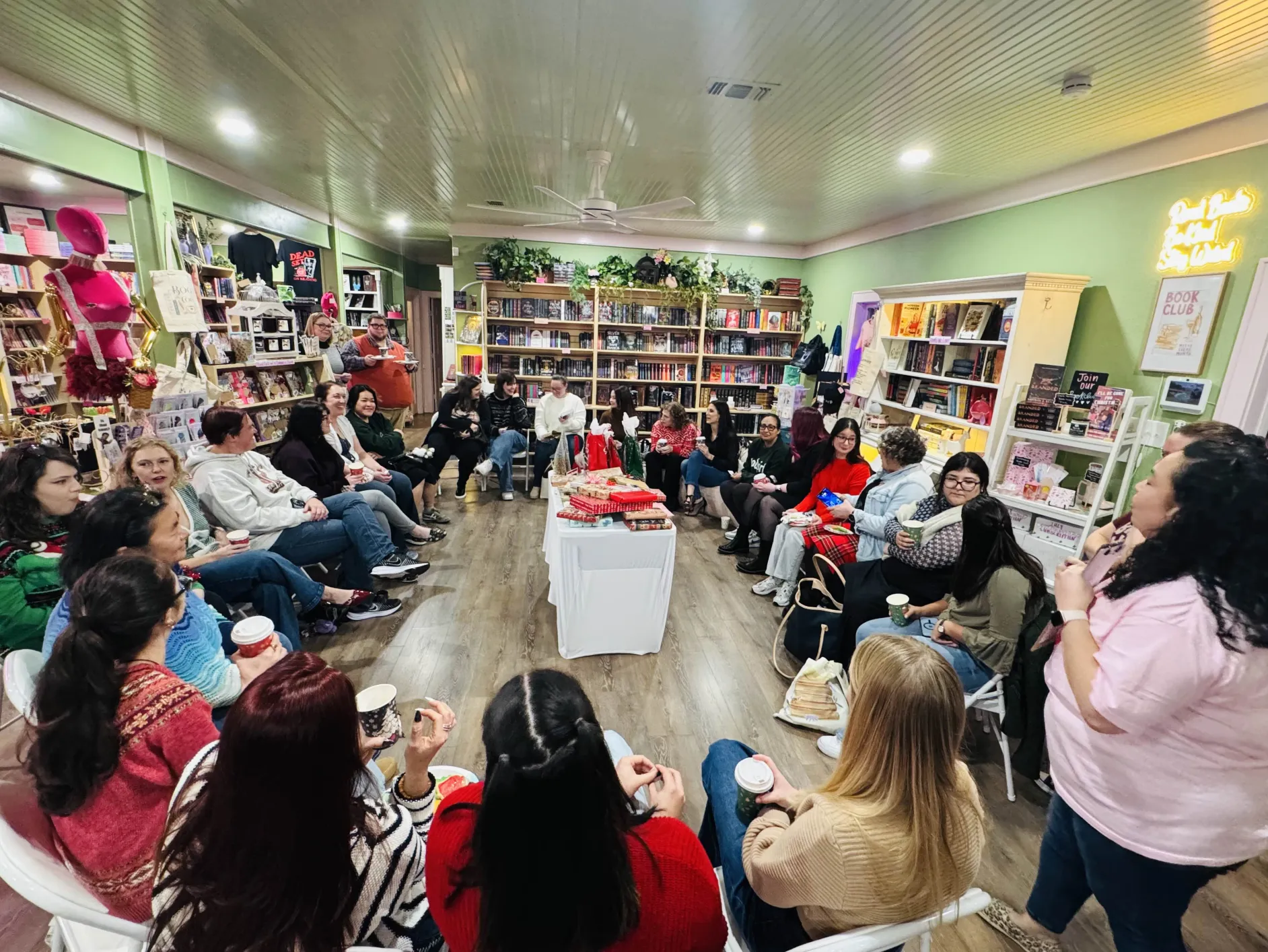 Group of people seated in a circle in a bookstore or library, engaging in a discussion or event, with bookshelves in the background.